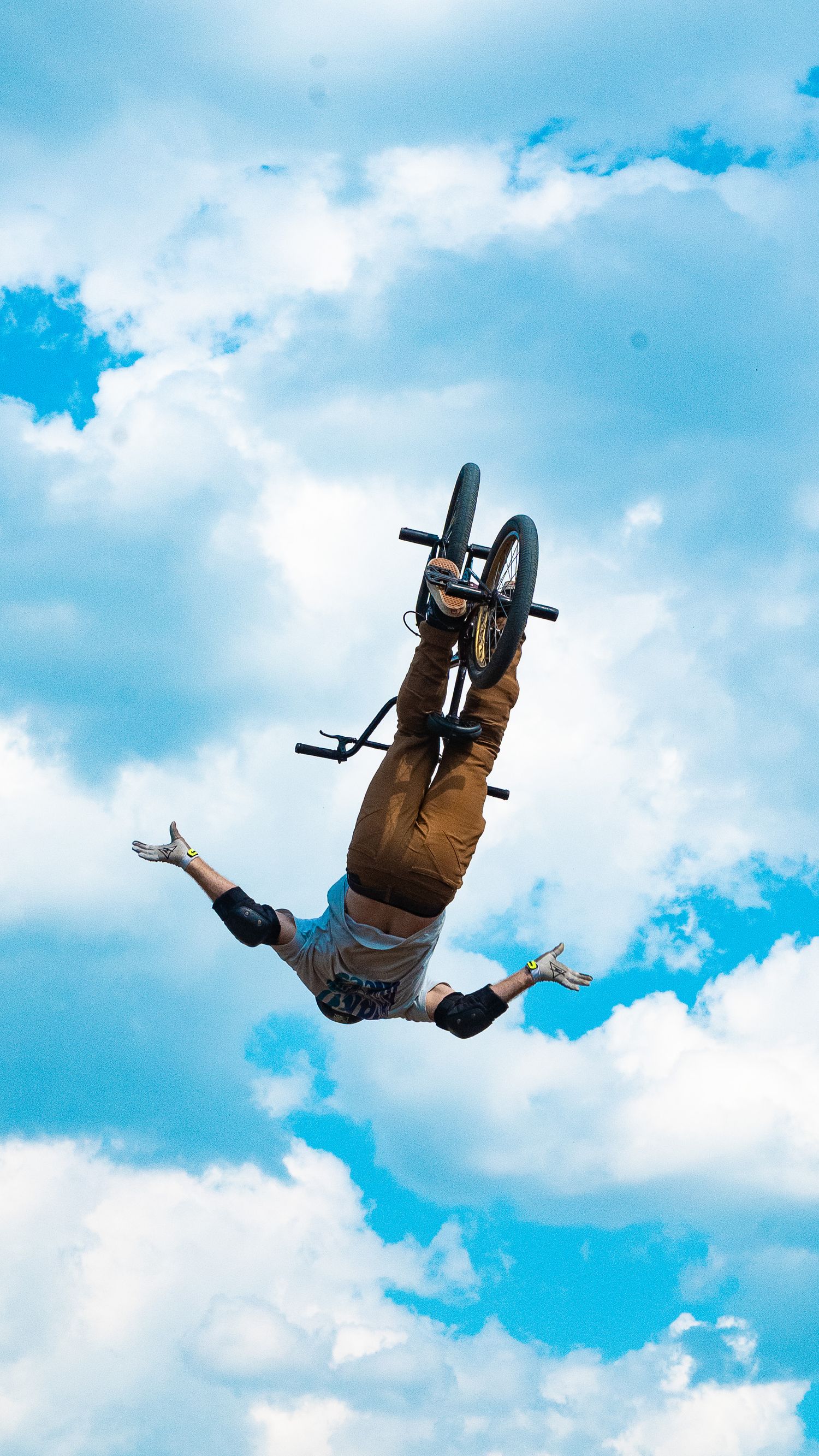 BMX rider flips upside down during aerial stunt with clouds in background.