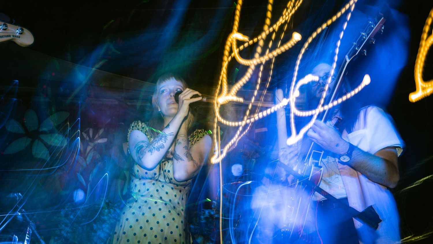 Concert performer sings on stage illuminated by dramatic blue lighting and neon effects.