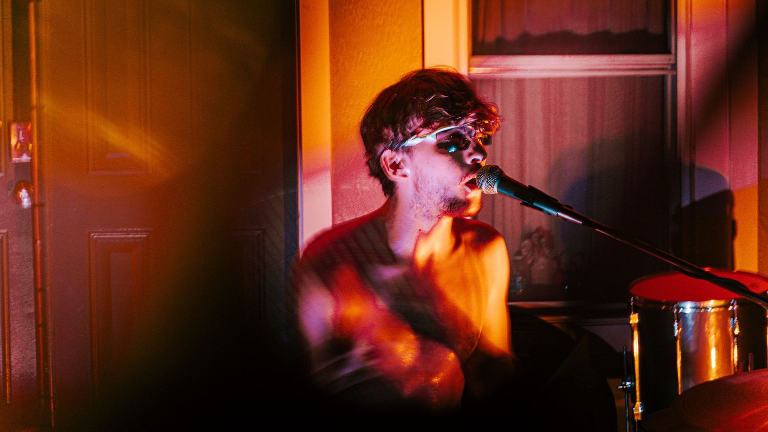 Concert performer singing into microphone with orange stage lighting creating moody atmosphere.