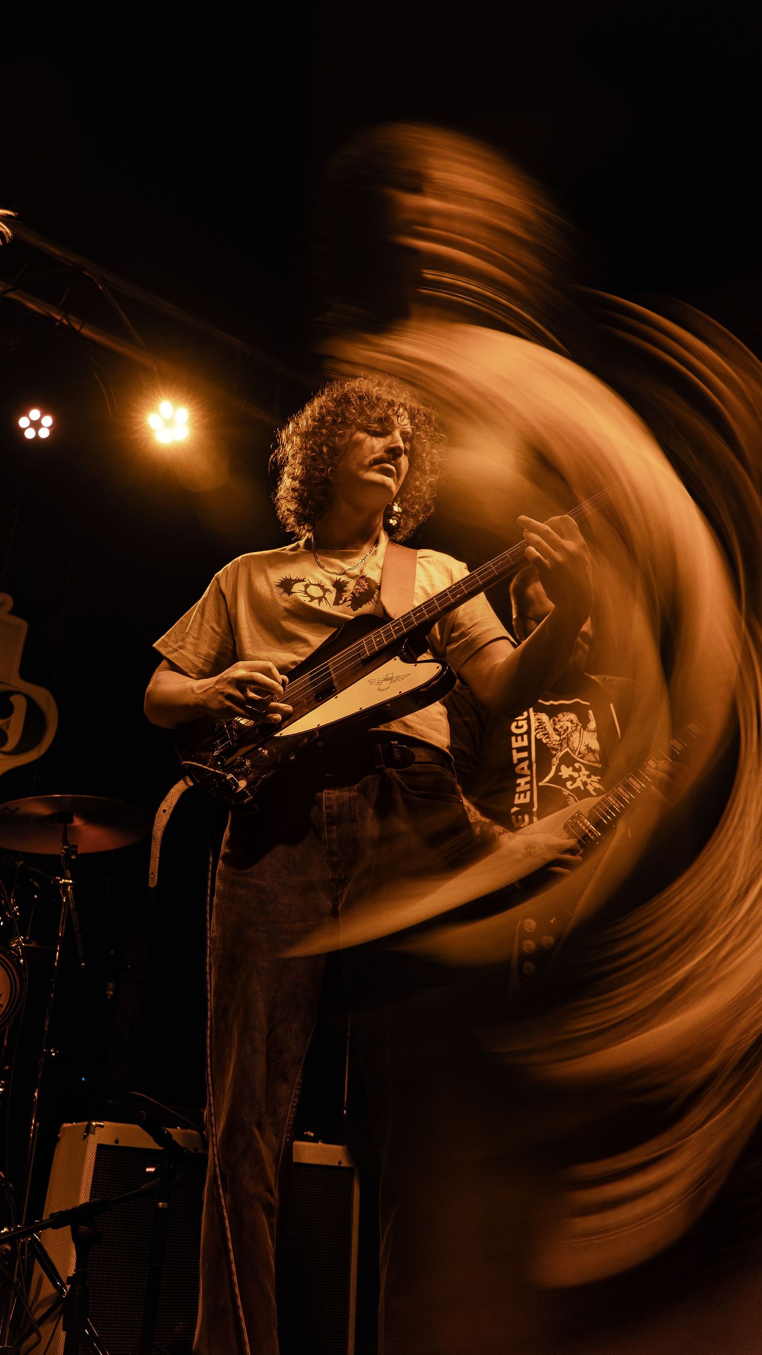 Dynamic motion blur captures a guitarist performing on stage in dramatic amber lighting and dark background.