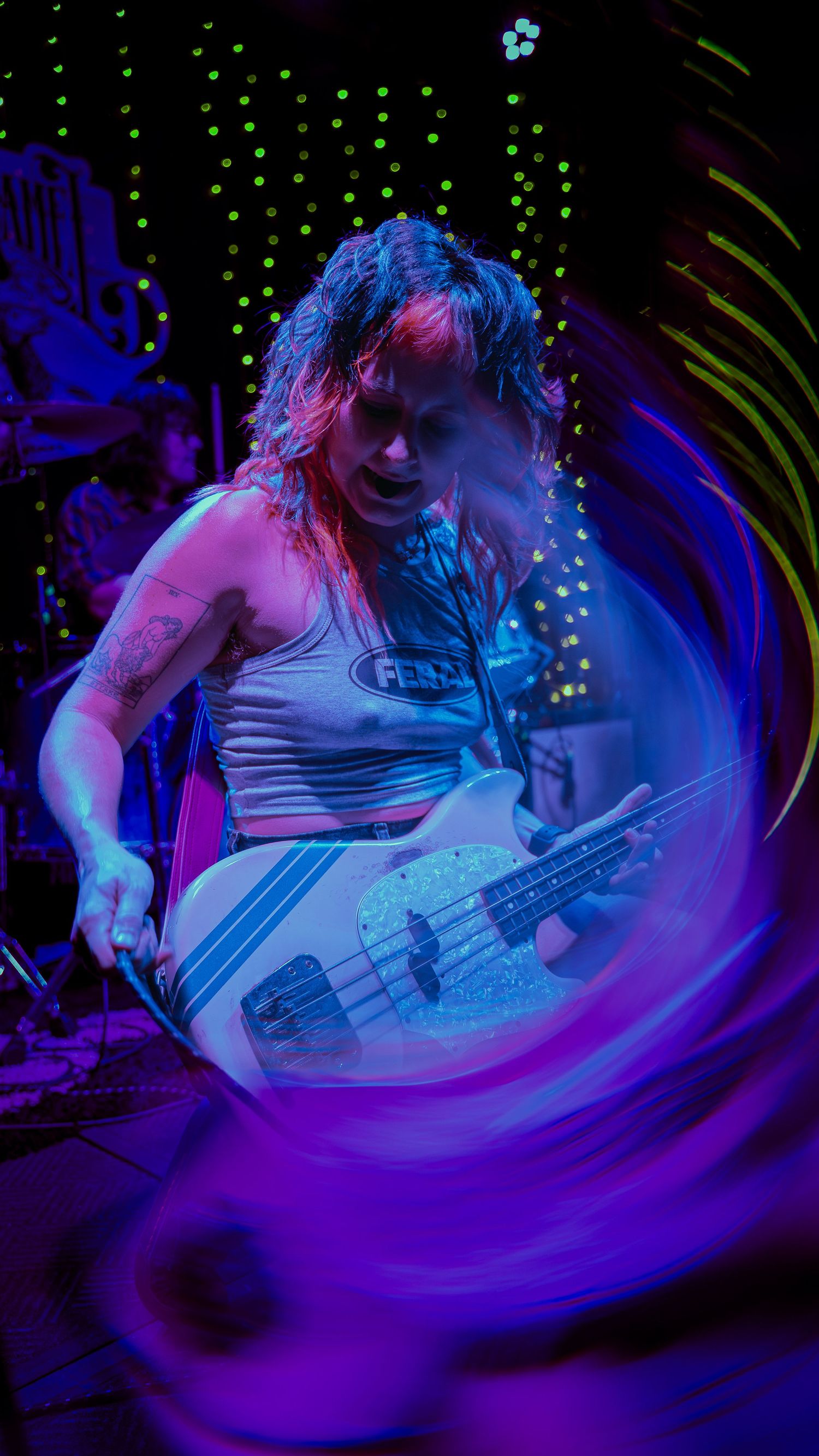A performer in white clothing plays an electronic instrument under dramatic blue and purple stage lighting creating motion trails.