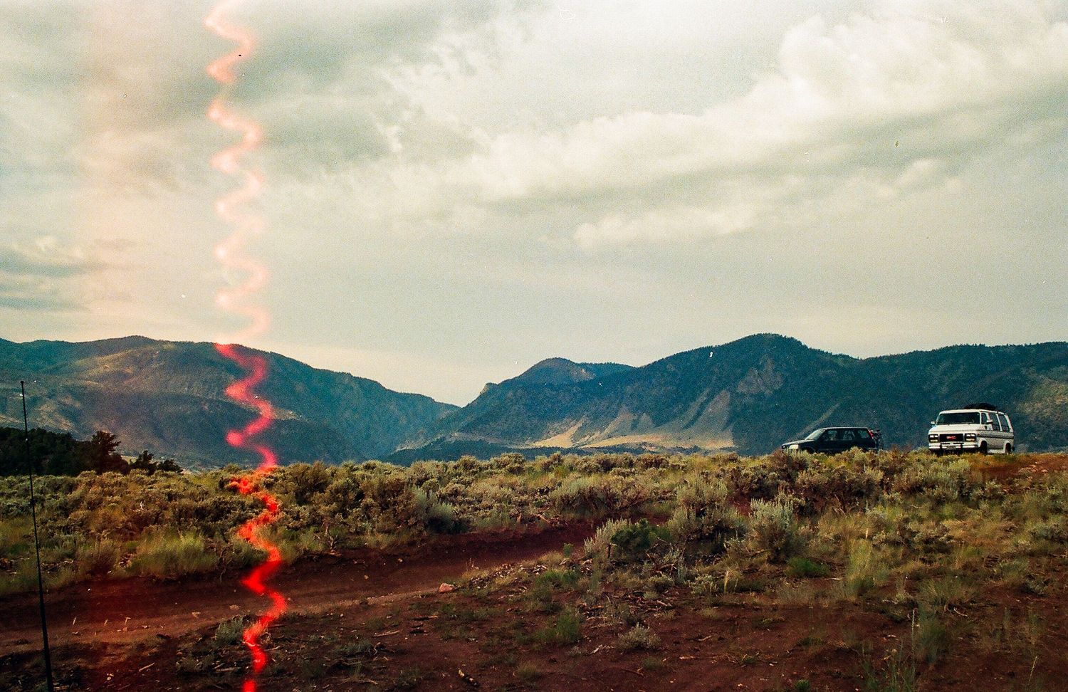 Desert landscape with mountains and a red light leak effect in the foreground.