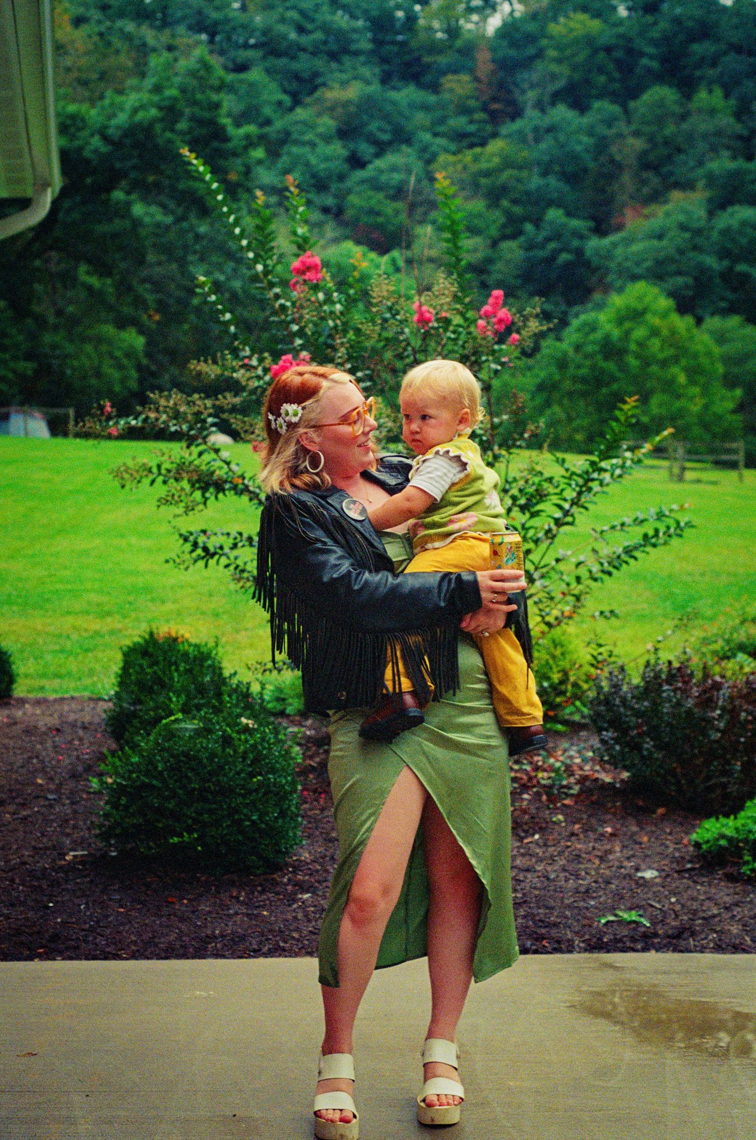 Two people share a playful moment in a lush garden setting with flowering shrubs and greenery.