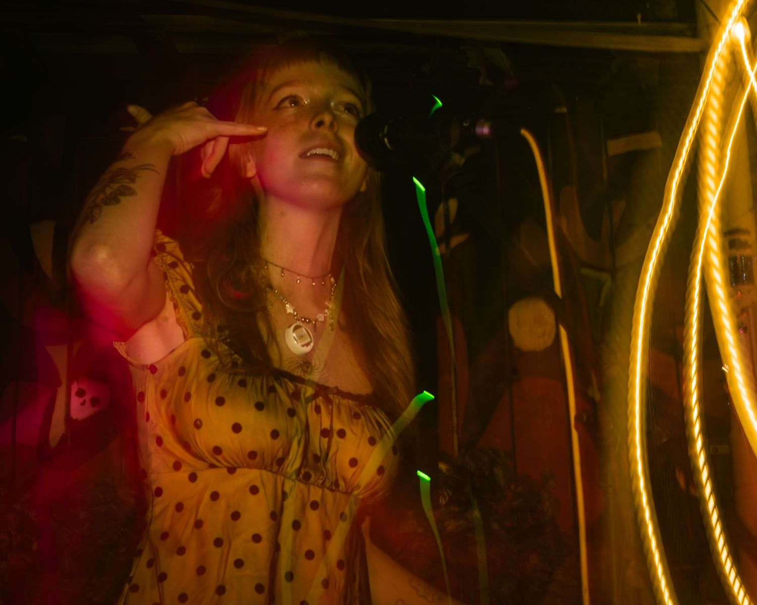 Stage performer in yellow polka dot dress singing under dramatic lighting effects.
