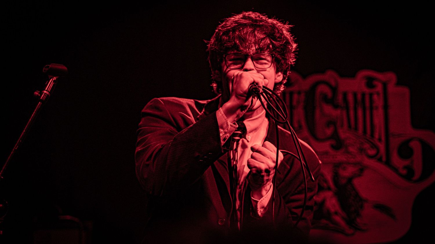 Concert performer singing passionately on dark stage with red dramatic lighting.
