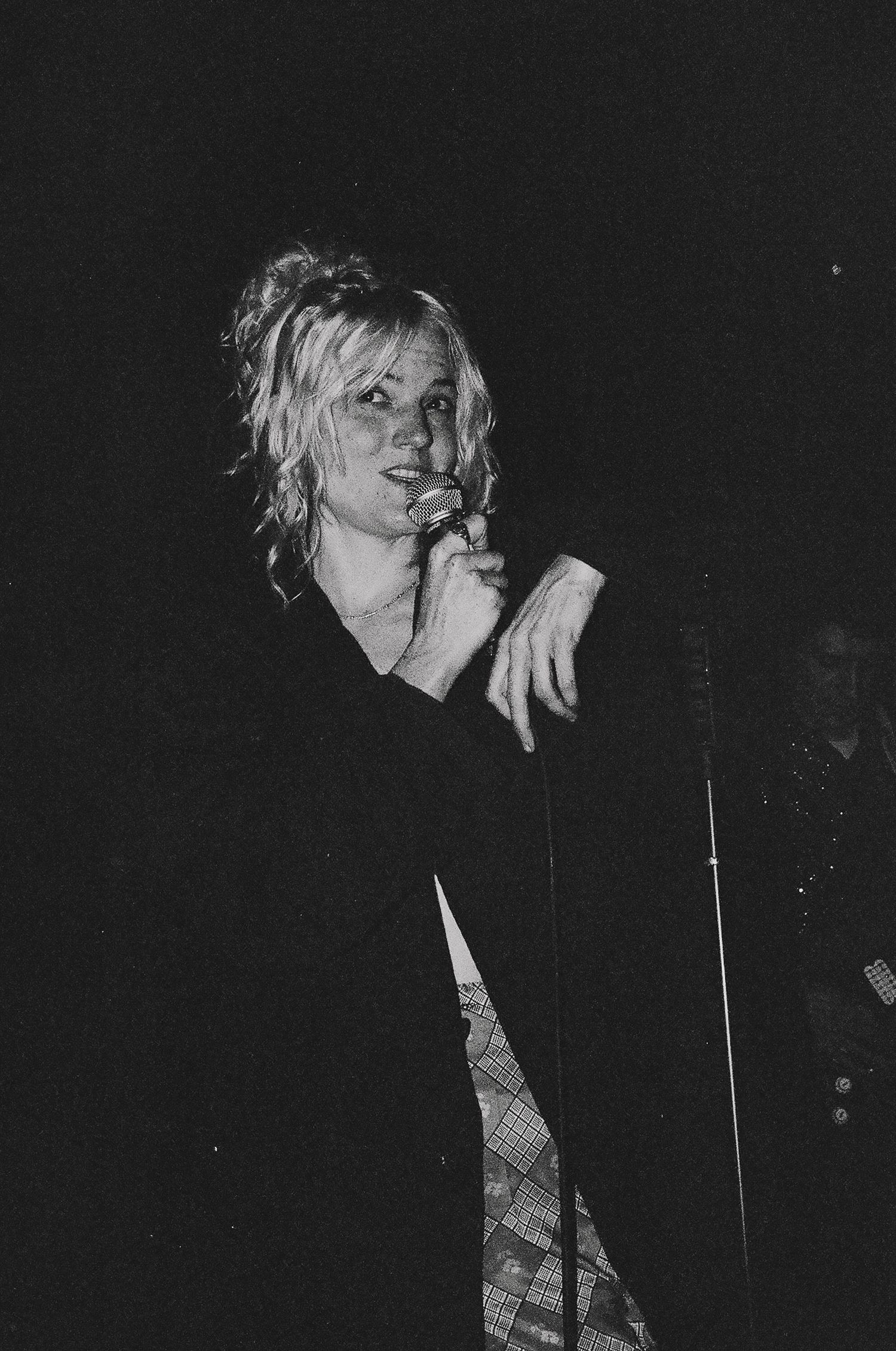 Grainy black and white photo of performer singing into microphone during nighttime concert.