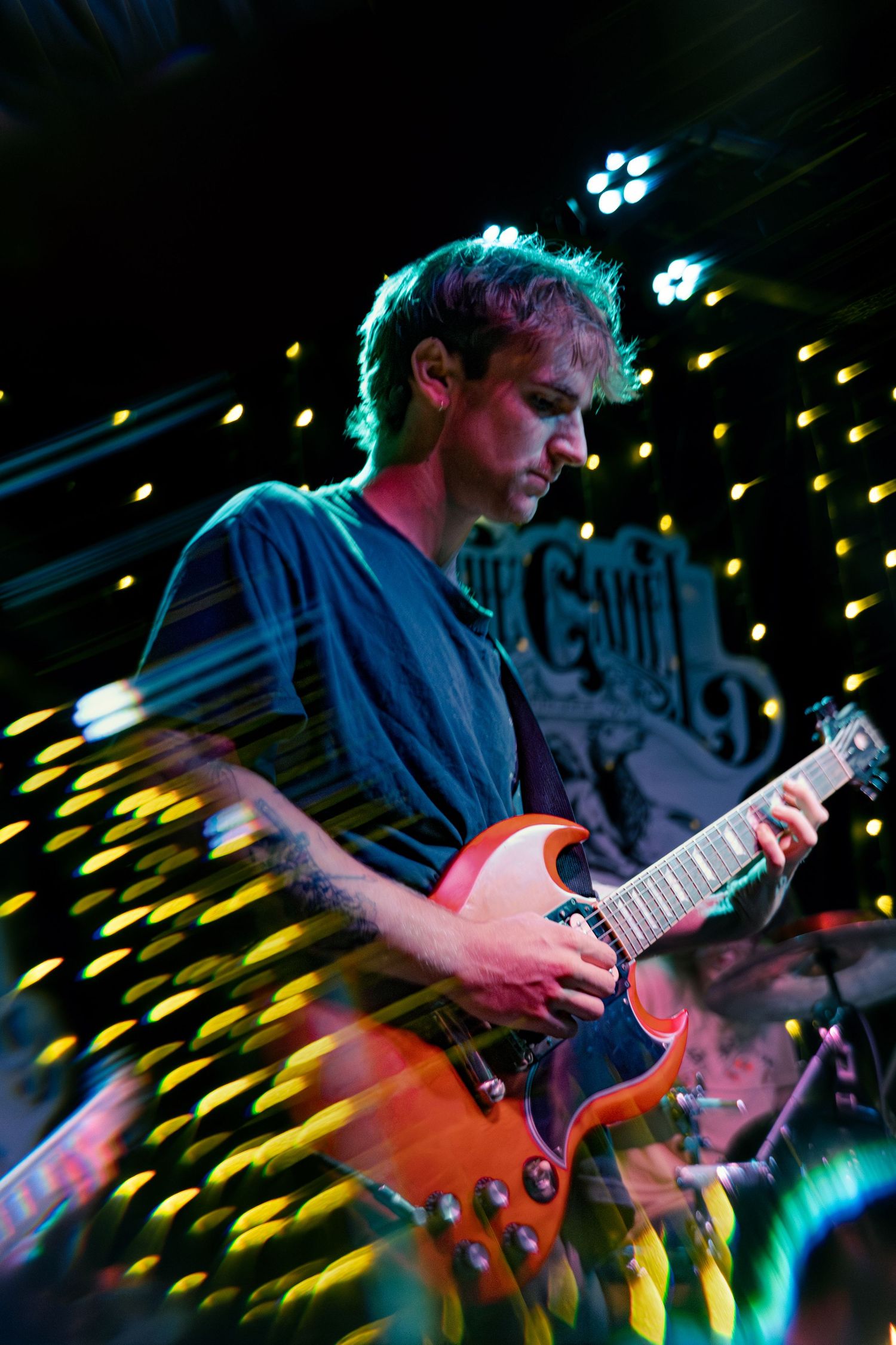 Guitarist performs energetically on stage with colorful yellow and blue stage lighting effects.