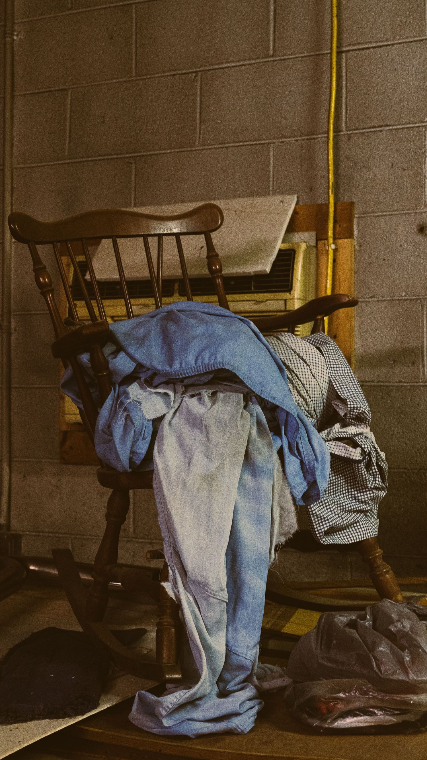 Blue fabric draped over wooden chairs in a dimly lit room with concrete block walls.