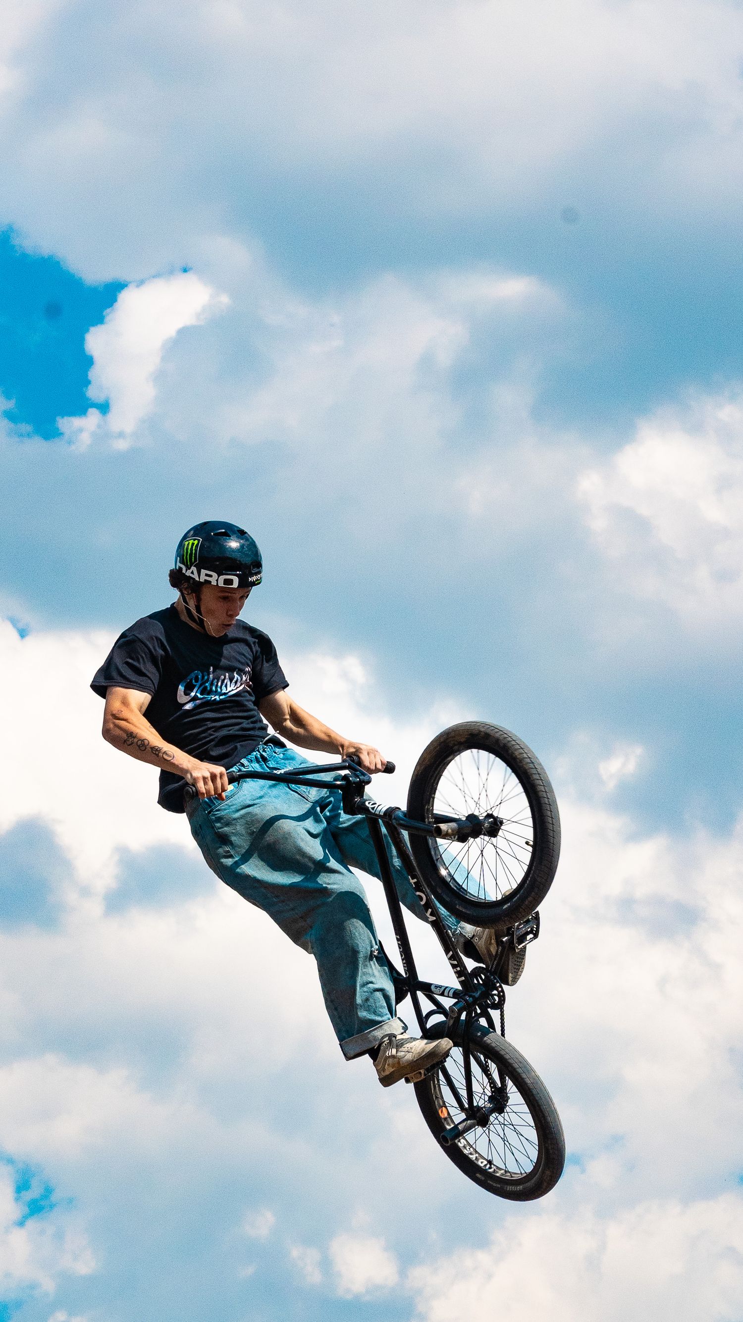 BMX cyclist performs aerial maneuver in mid-flight against cloudy blue sky.