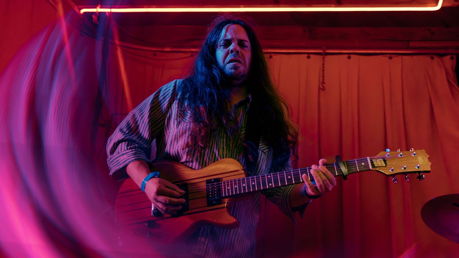 Live music performer playing acoustic guitar under moody red stage lighting during an intimate concert performance.