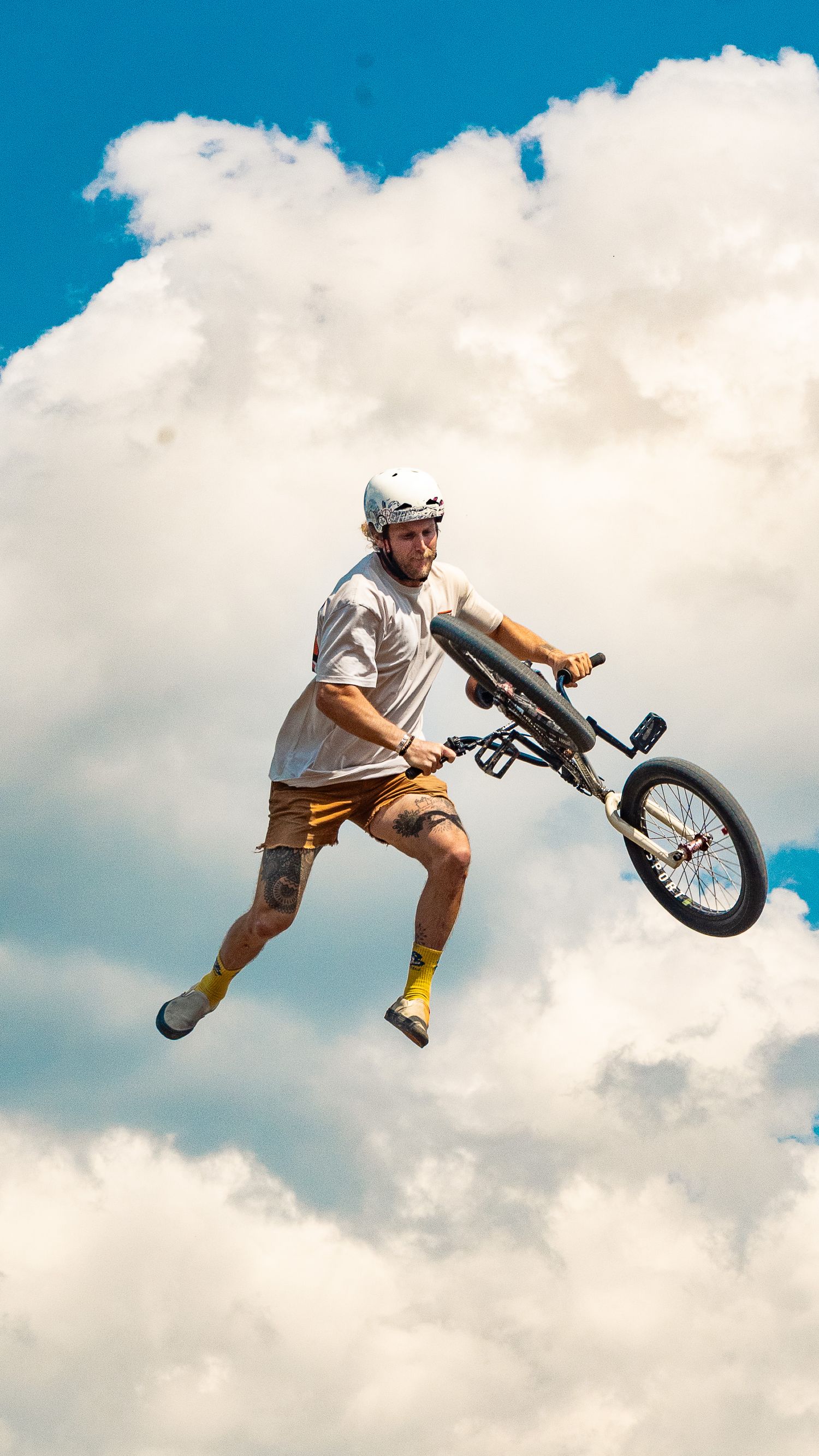 BMX rider performs impressive aerial stunt against blue sky and white clouds.