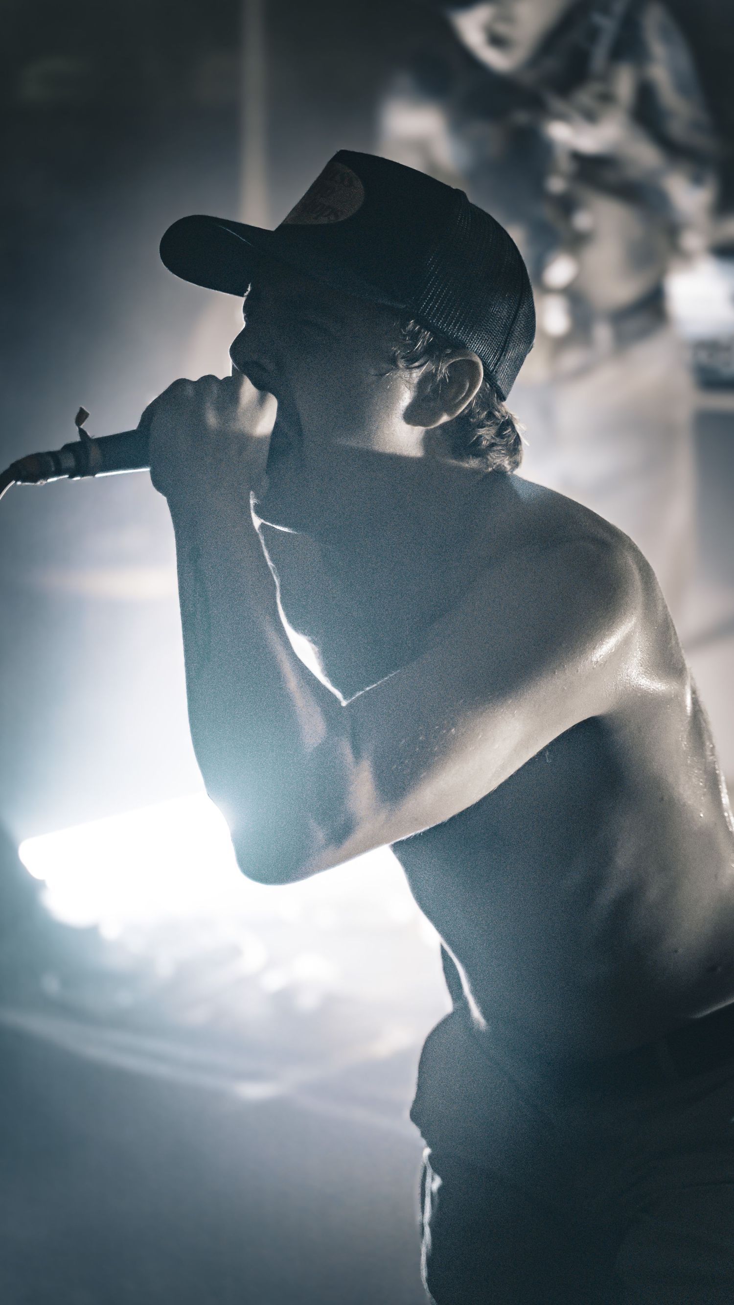 Silhouetted side profiles of performer against bright stage lighting in moody concert atmosphere.