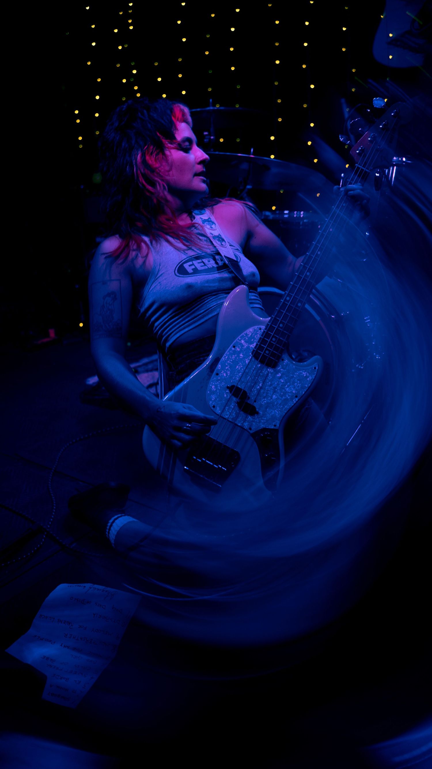 Musician performing on acoustic guitar under dramatic blue and purple stage lighting during a nighttime concert.