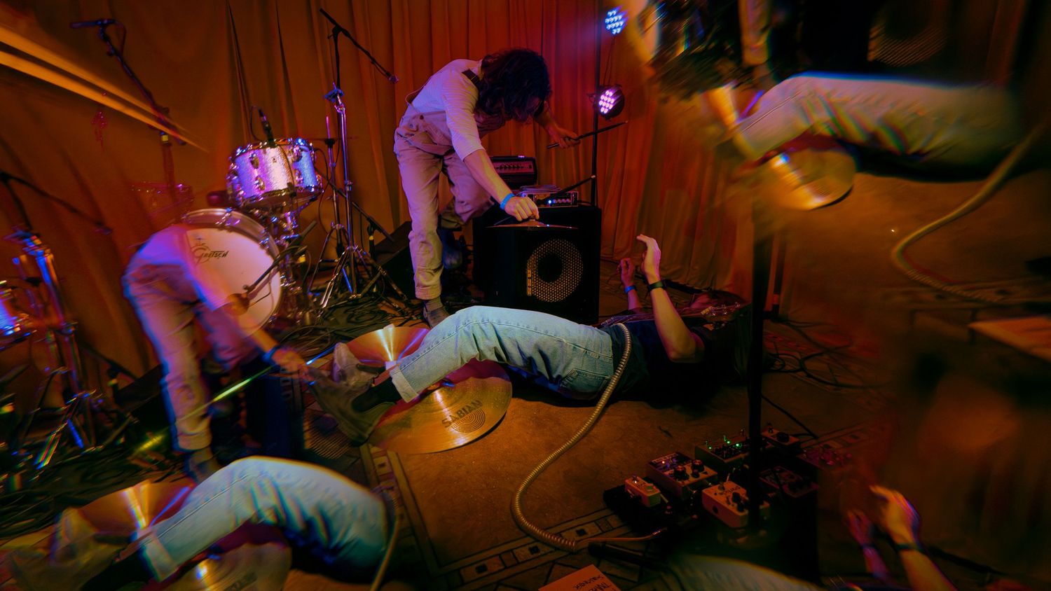 A large crowd dances energetically in a dimly lit club atmosphere with colorful lighting effects.