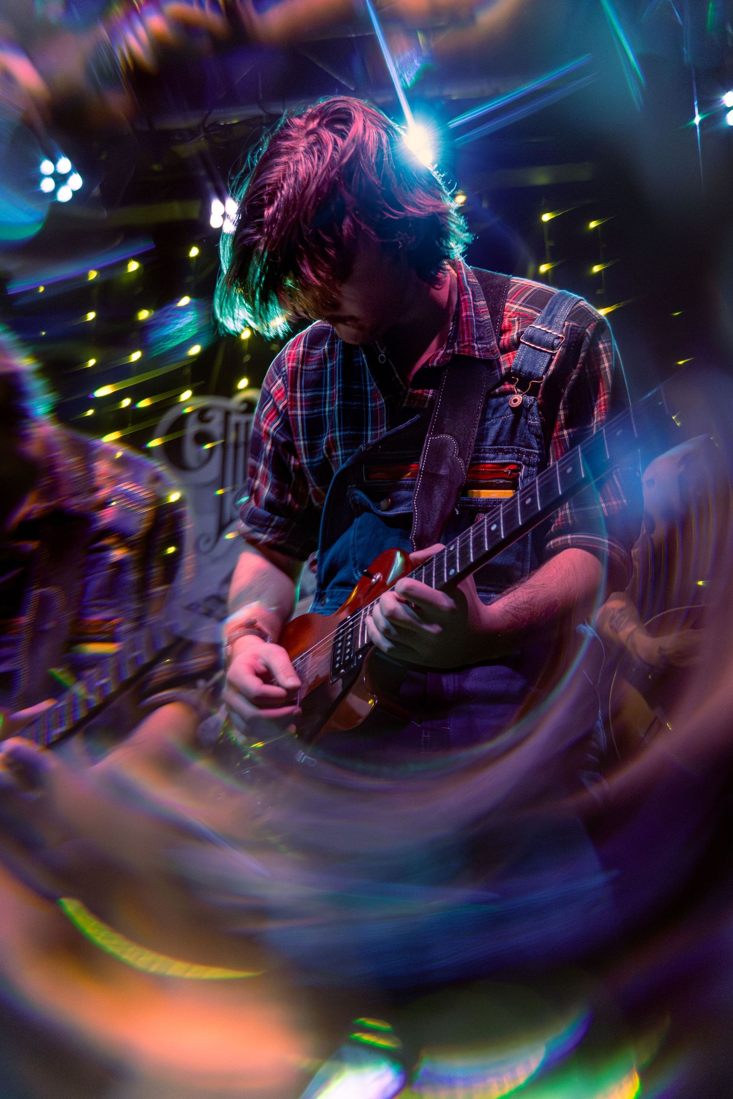 Guitarist performing on stage with colorful lighting effects and motion blur creating dynamic concert atmosphere.