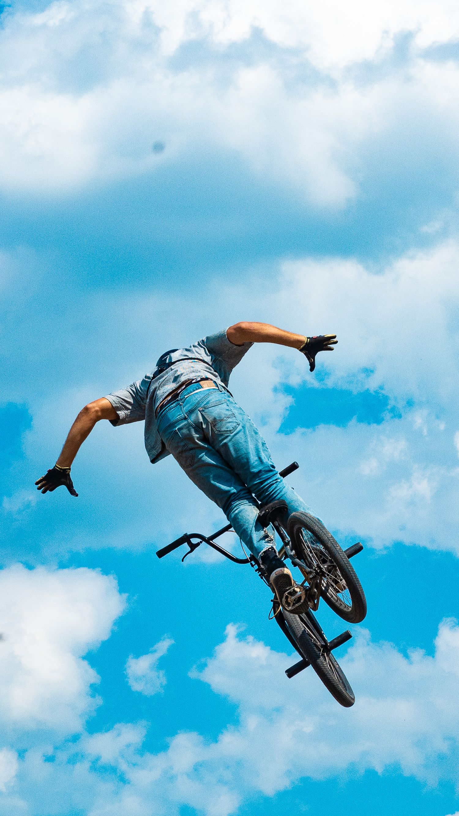 BMX athlete performs horizontal aerial maneuver against cloudy sky background.