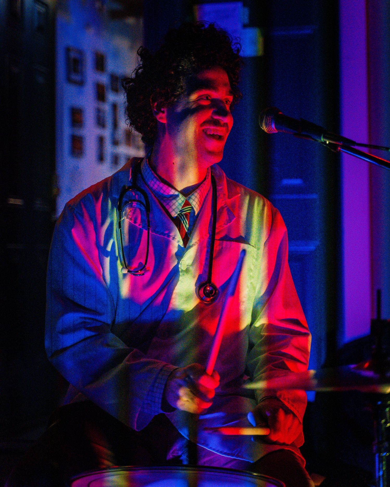 Musician in colorful attire performing under blue and red stage lights at a concert venue.