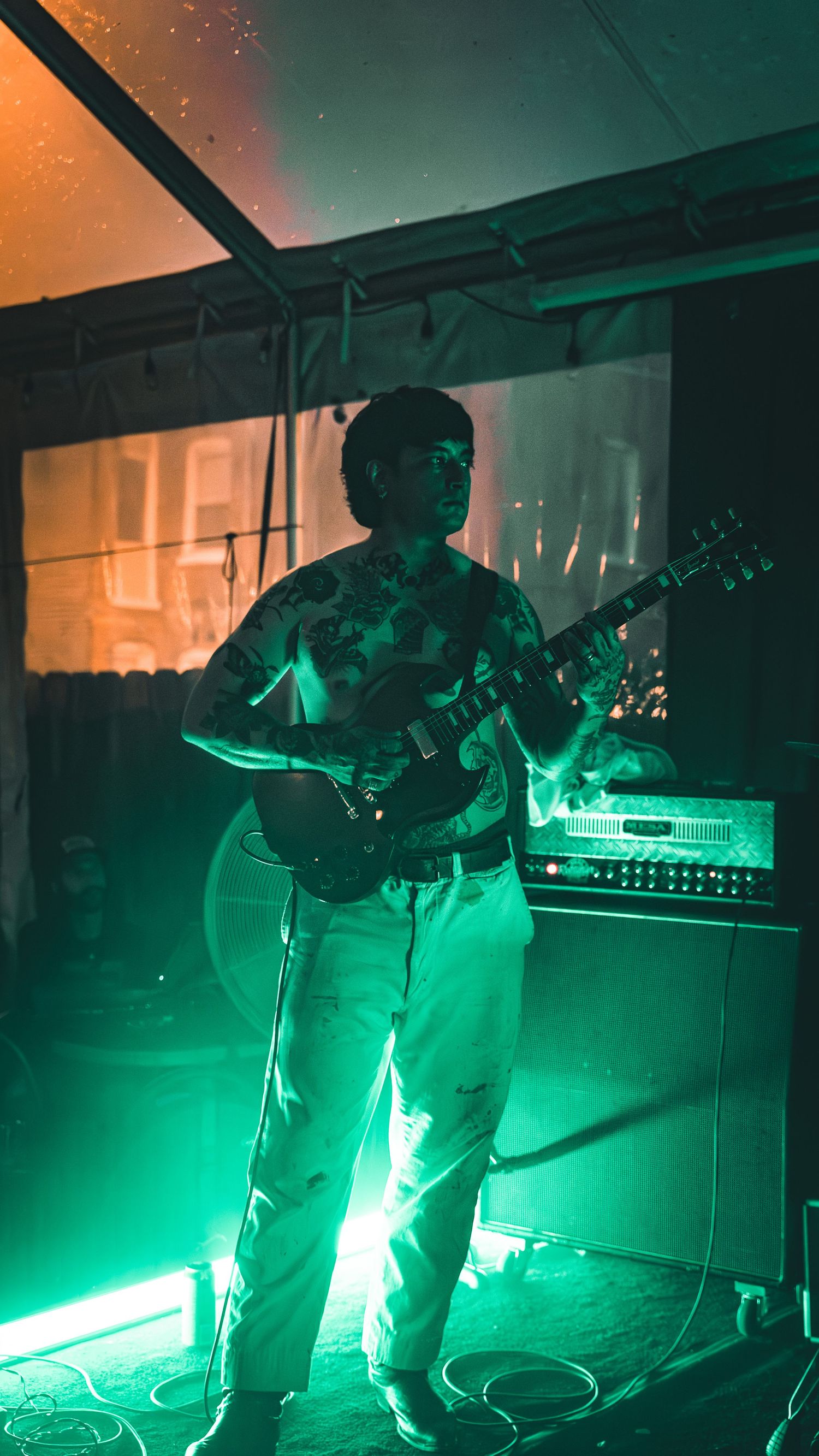 A musician performs under dramatic green stage lighting while holding musical equipment.