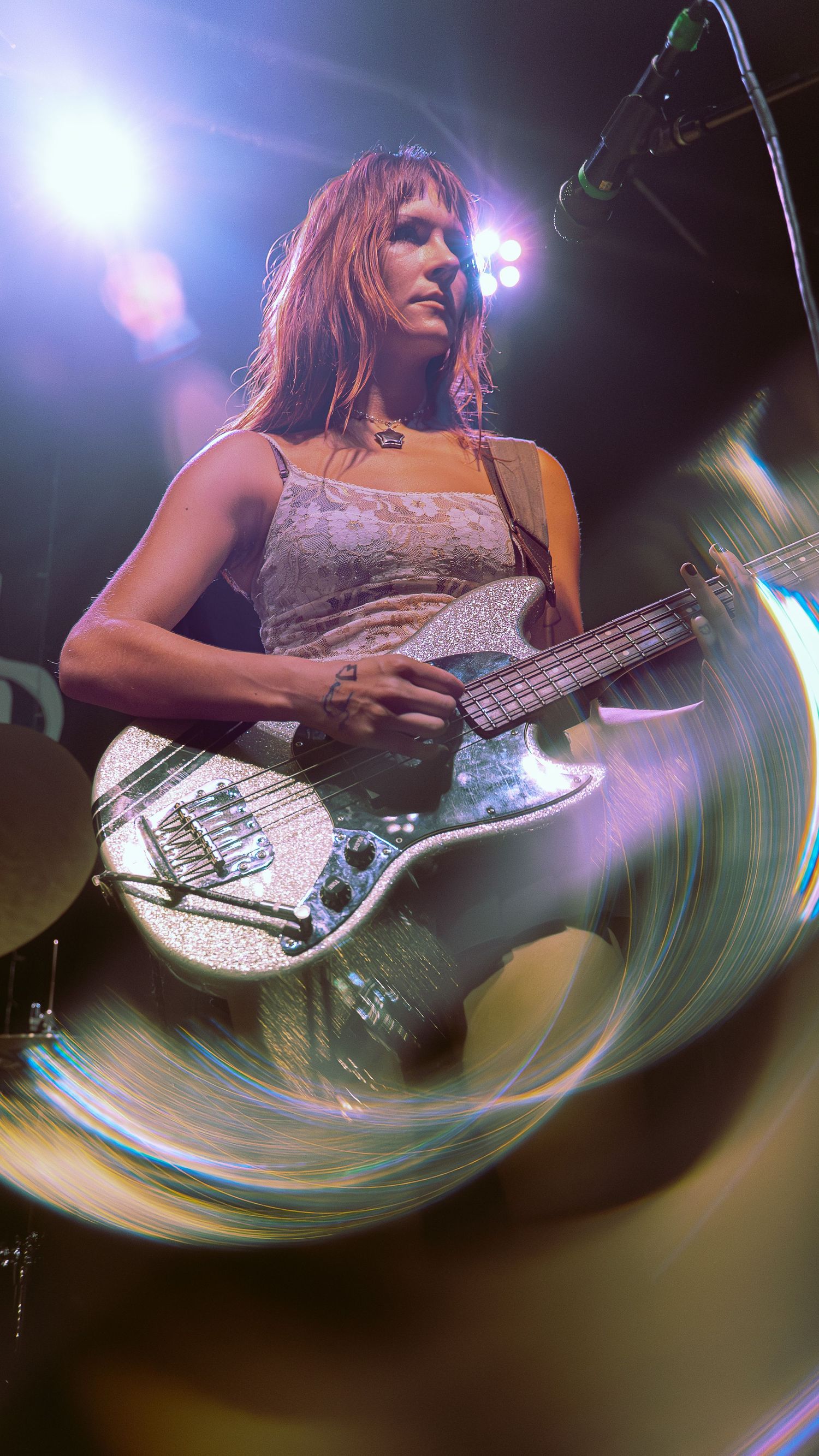 A bass guitarist performs on stage under dramatic lighting with a swirling lens effect creating a dynamic visual motion.