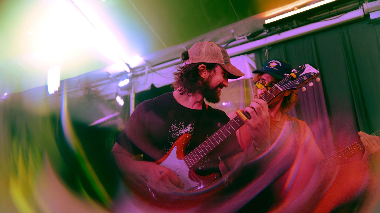 Musicians perform on stage with colorful green and red lighting effects creating a dynamic concert atmosphere.
