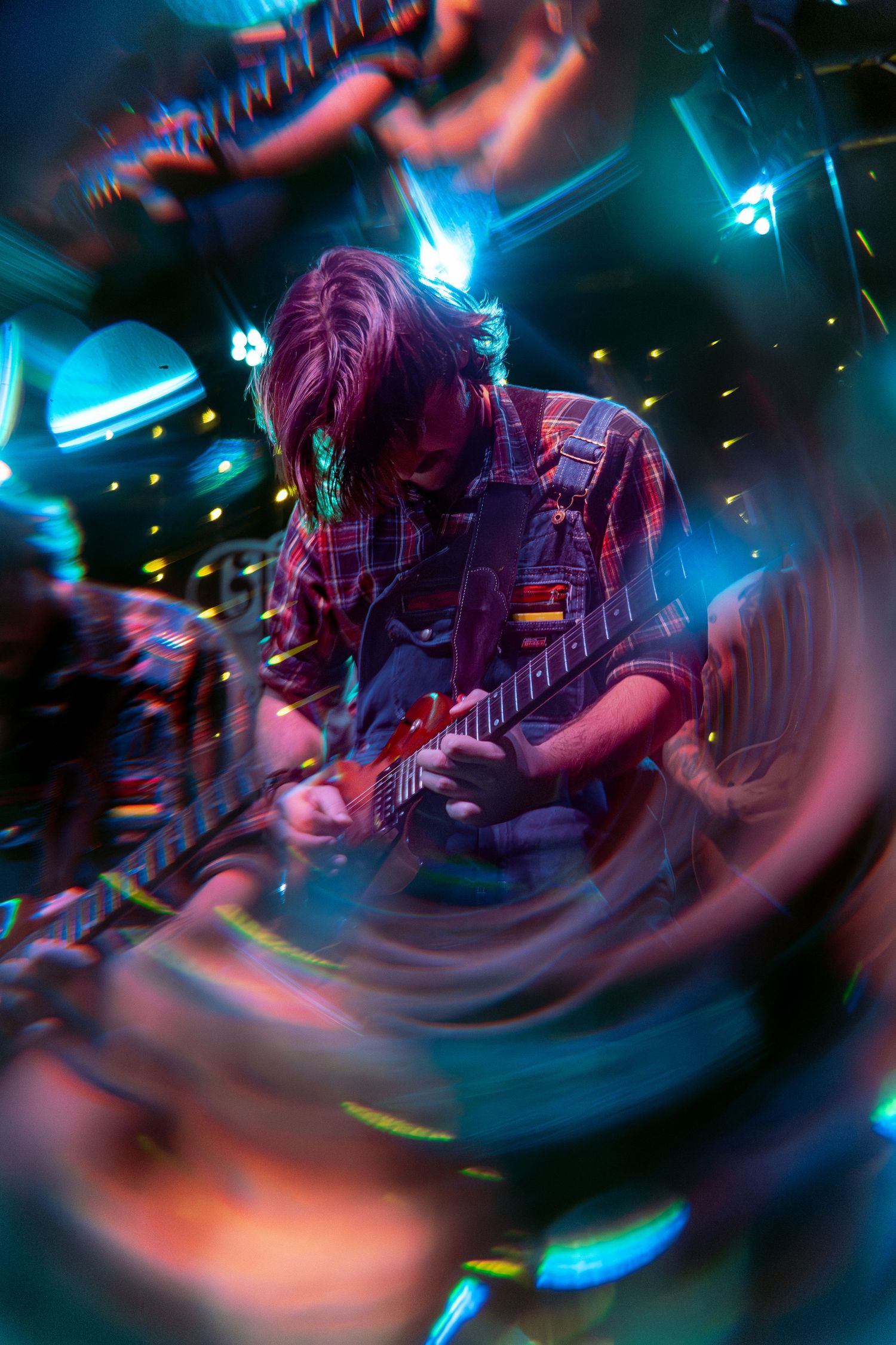 Dynamic motion-blur photograph of guitarist performing onstage with dramatic blue and red stage lighting.