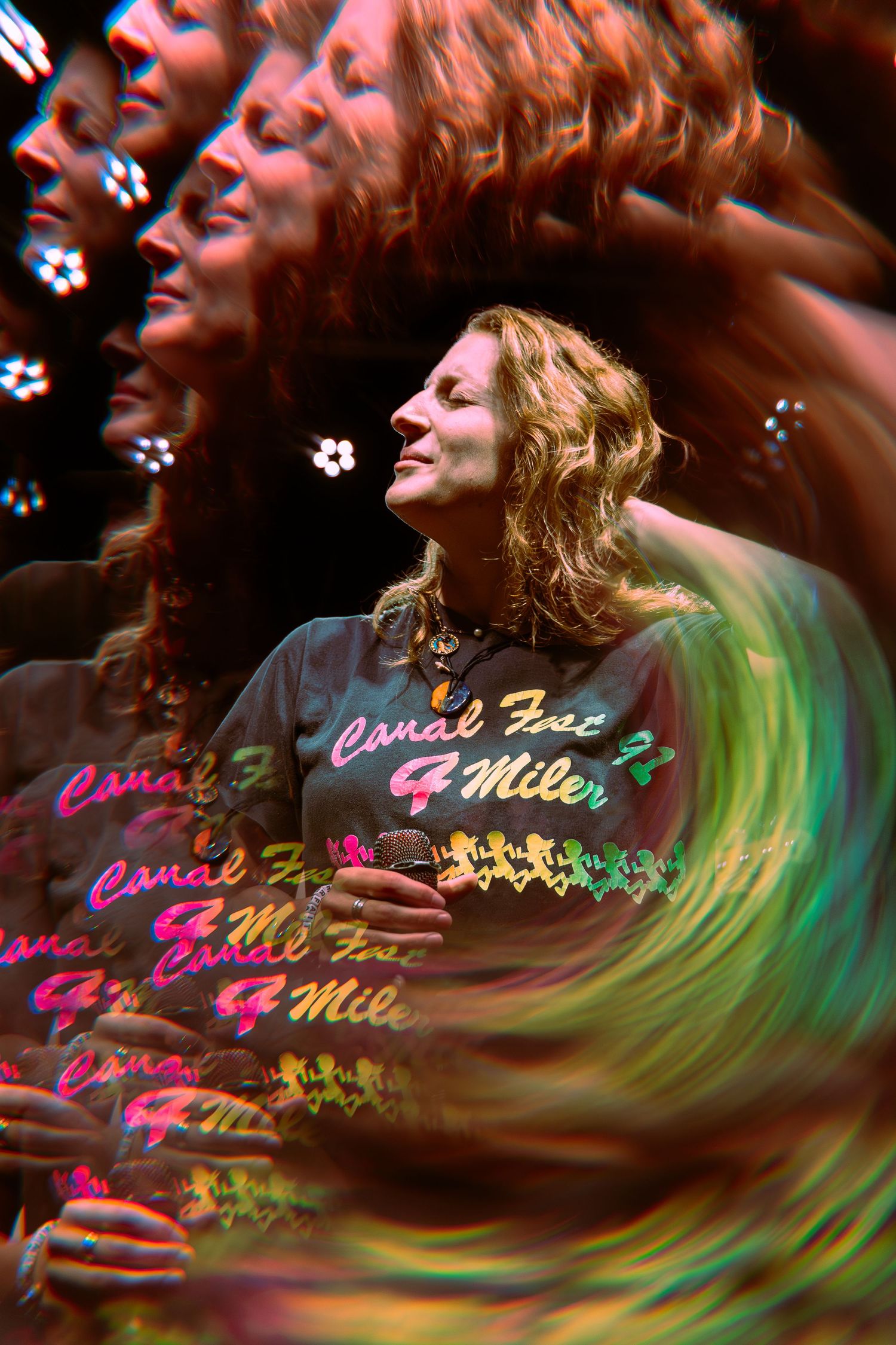 Multiple exposure photo shows motion blur of someone performing with vibrant green and pink lighting effects on stage.
