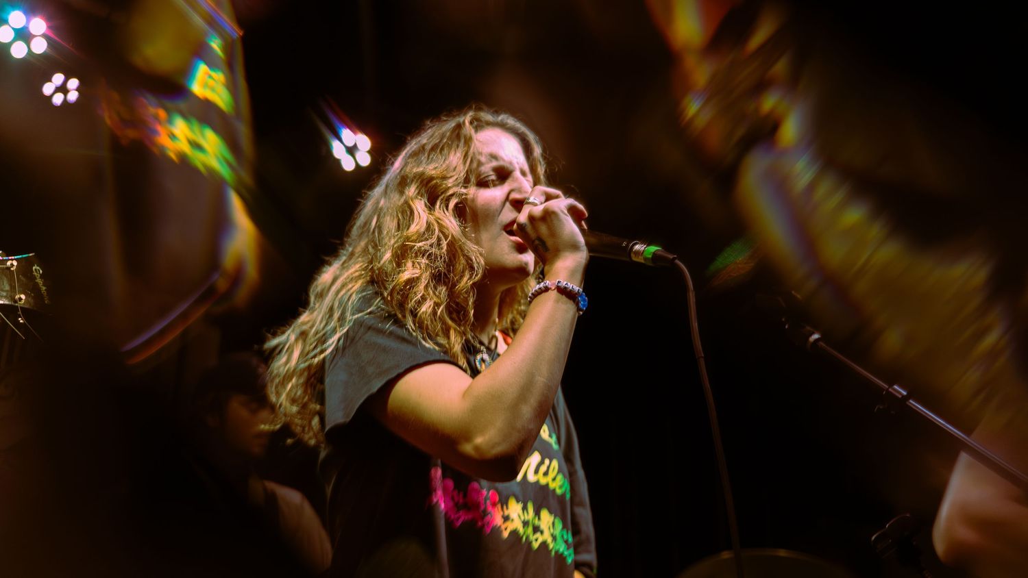 Colorful concert stage lighting illuminates a performer singing passionately with dramatic lighting effects in background.