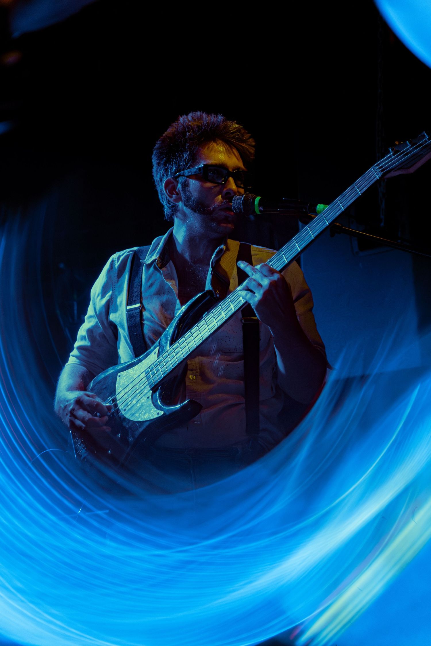 Guitar player performs under vibrant blue stage lighting creating dynamic motion blur effects during live concert.
