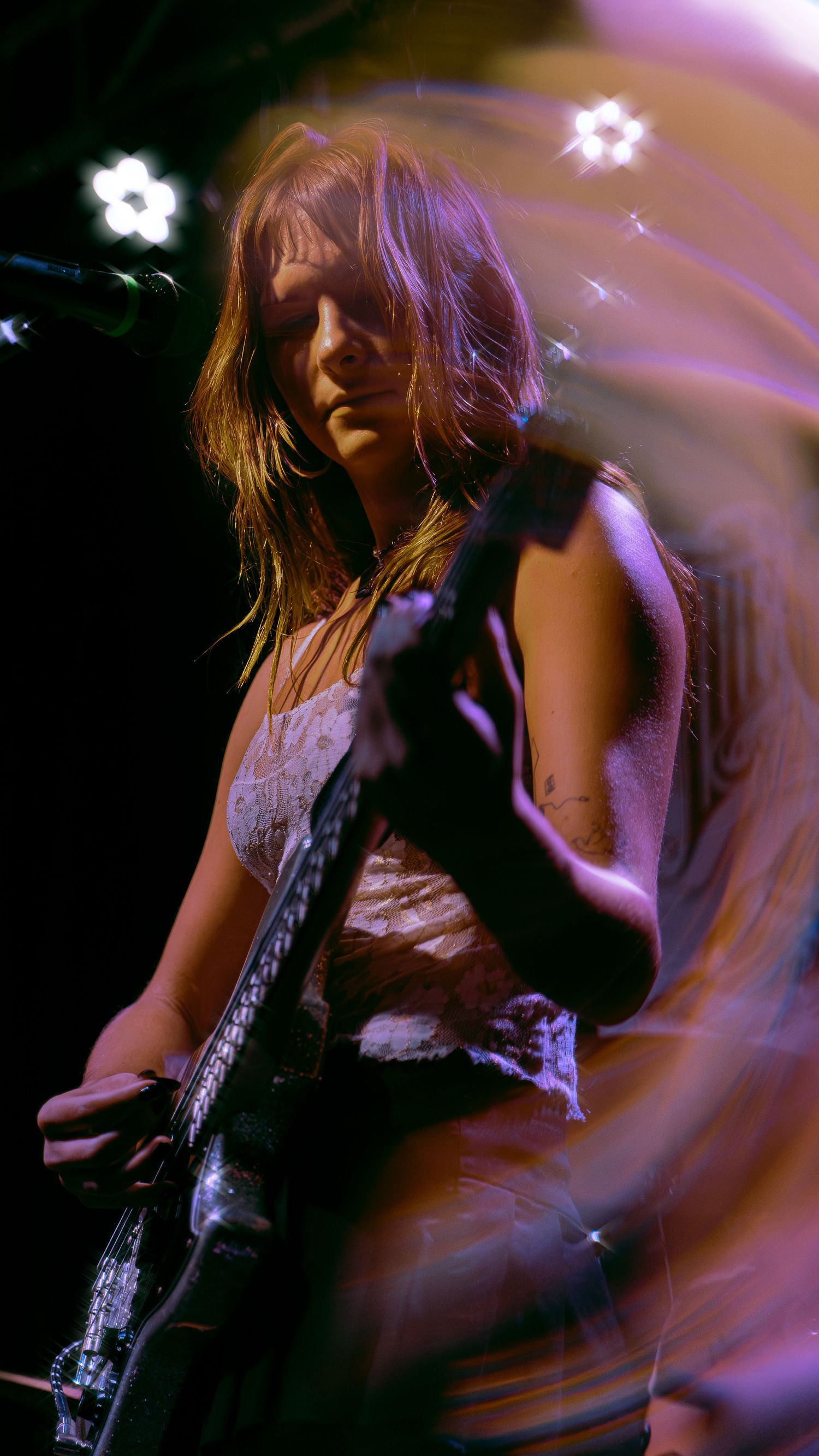 A musician performs on stage with a guitar under purple stage lighting, creating a dreamy atmospheric effect.