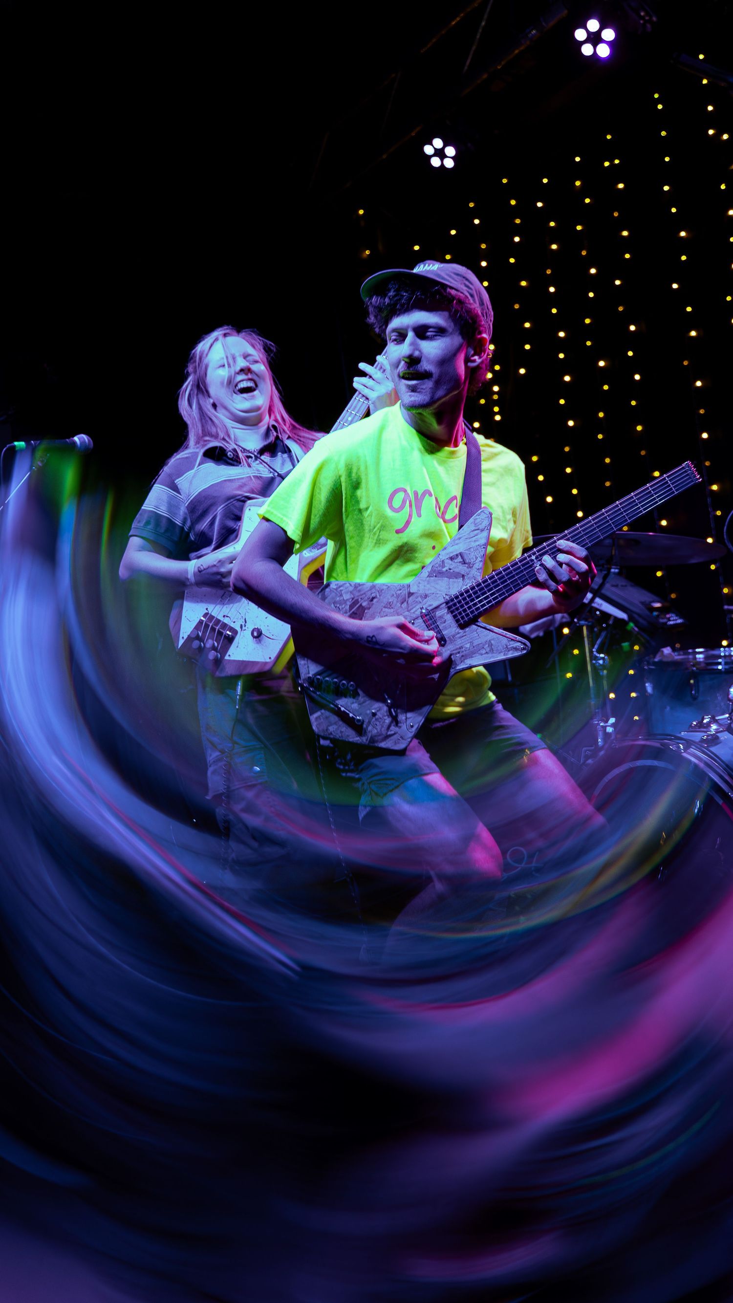 A dynamic performance shot showing musicians playing guitar in neon lighting with a swirling motion blur effect.