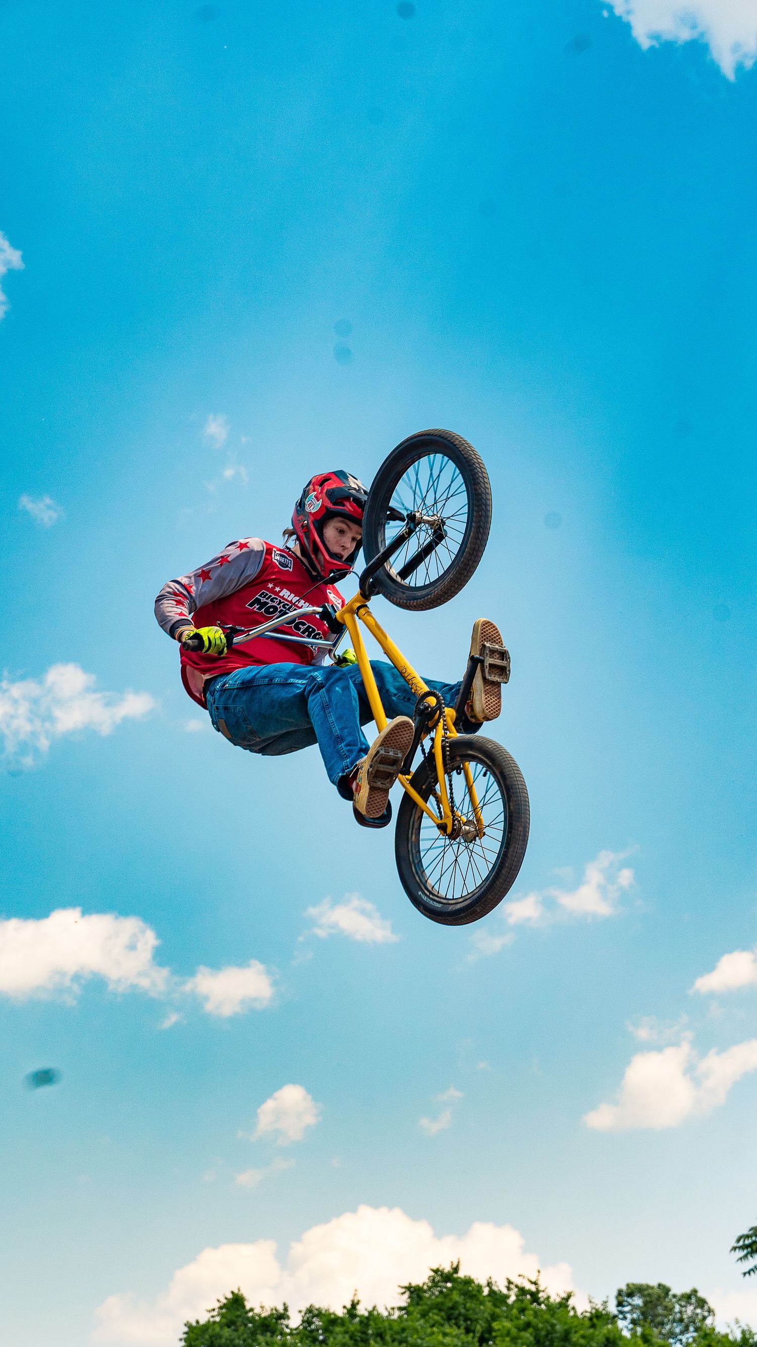 BMX rider in red performs backflip trick against bright blue sky.