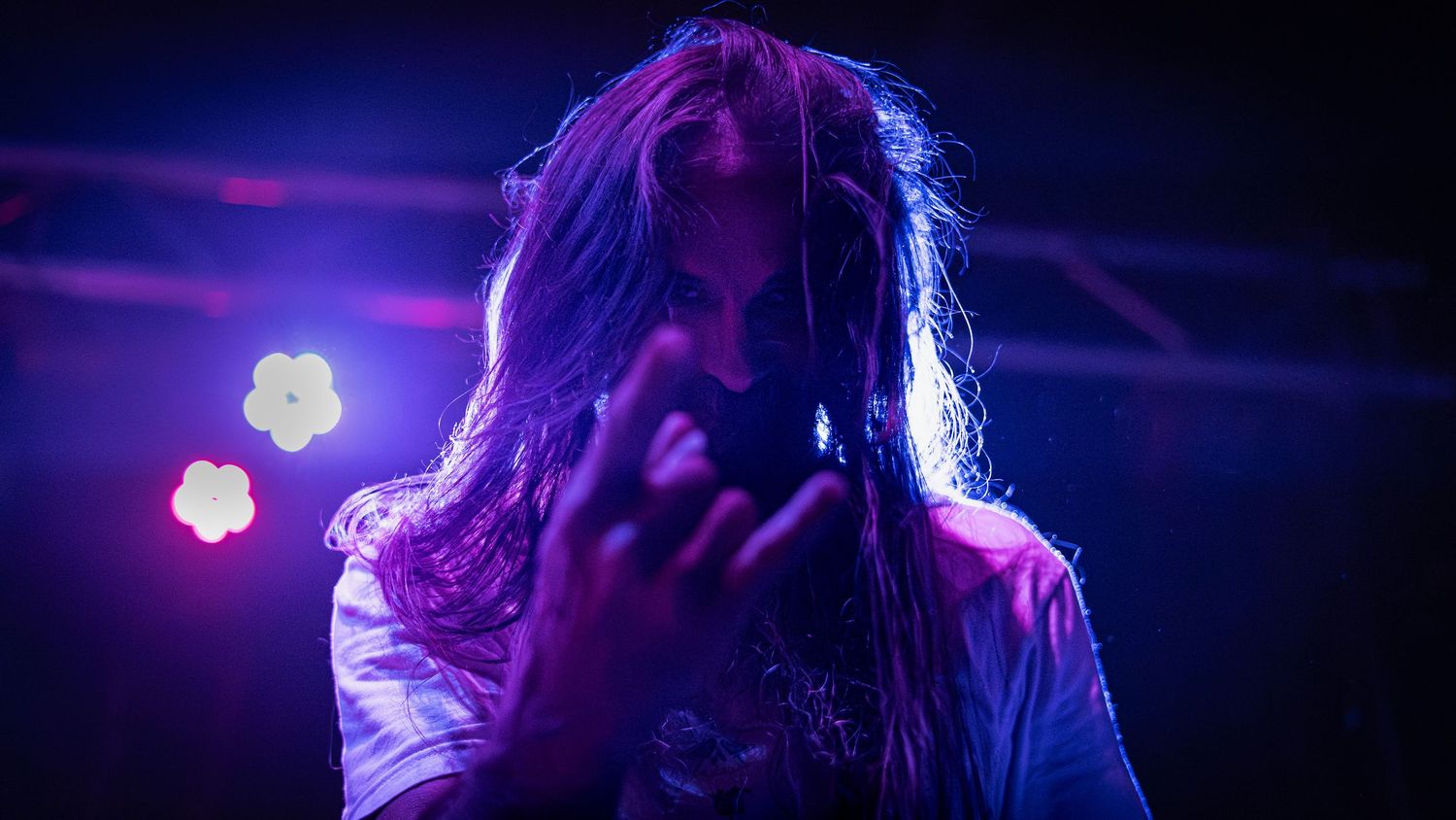 A performer silhouetted against purple stage lighting performs passionately at a concert.