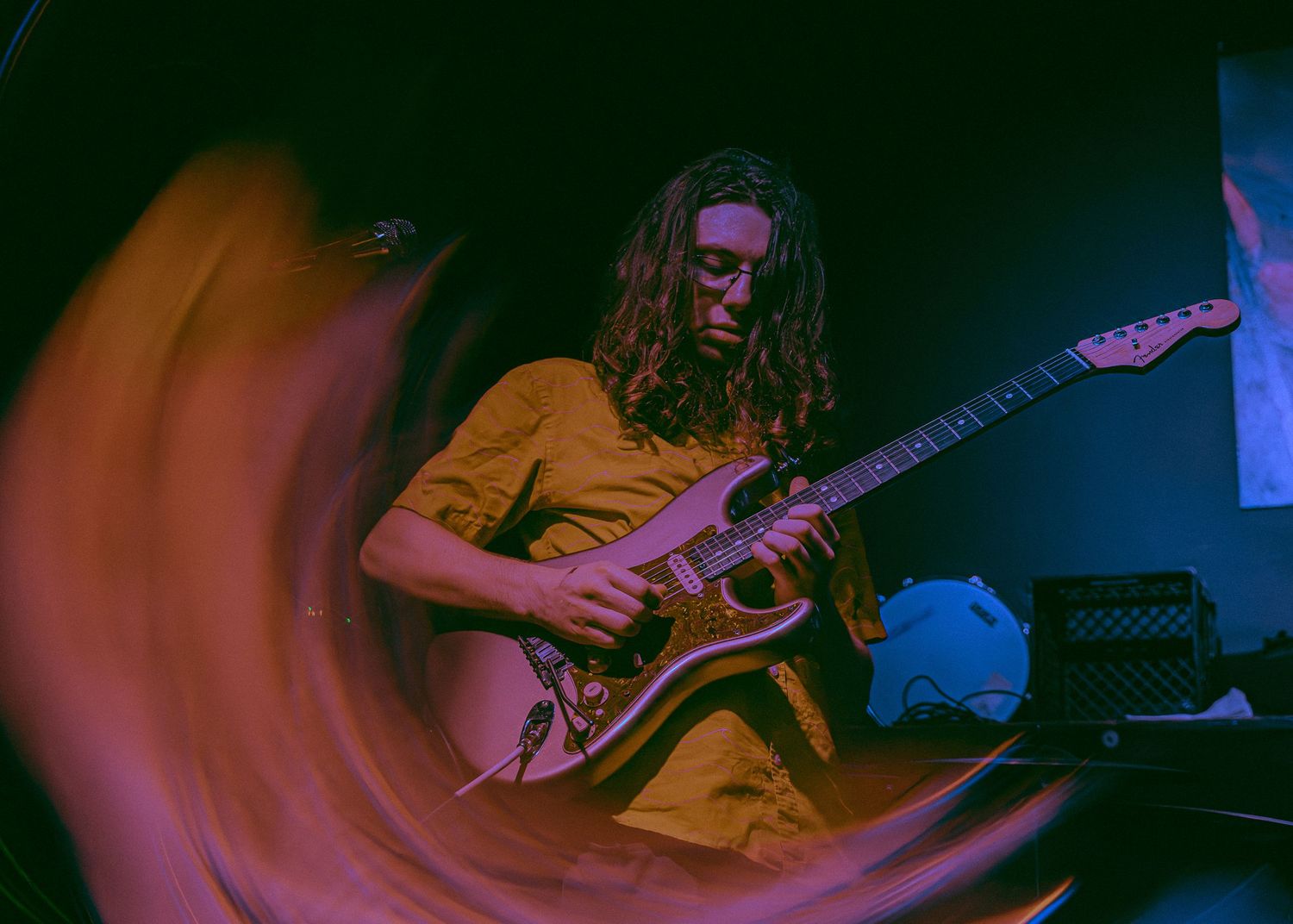 A guitarist in a yellow shirt performs on stage with motion blur effects and colorful lighting.
