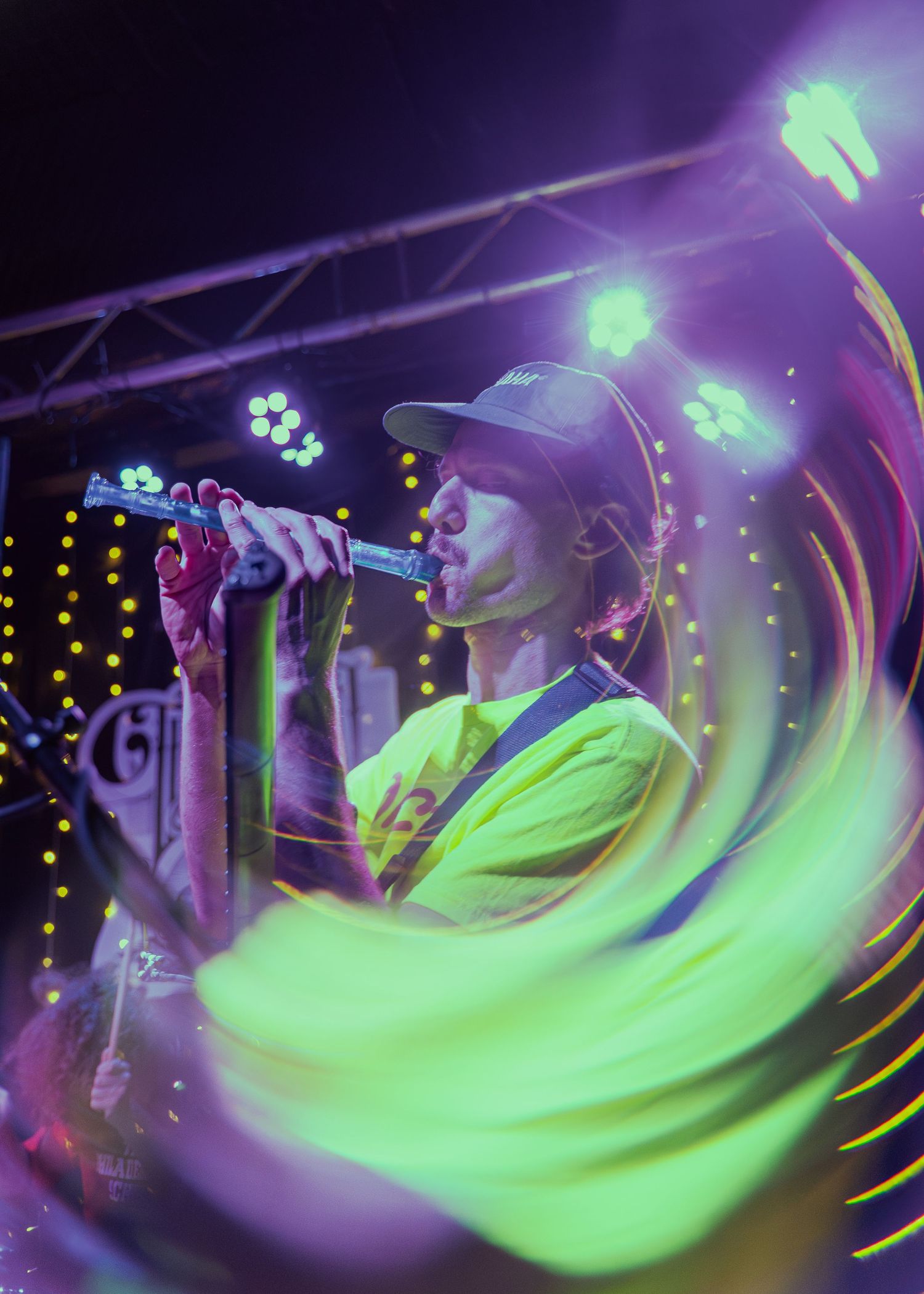 Performer in neon yellow shirt sings on stage with dynamic motion blur and purple lighting effects at a concert venue.