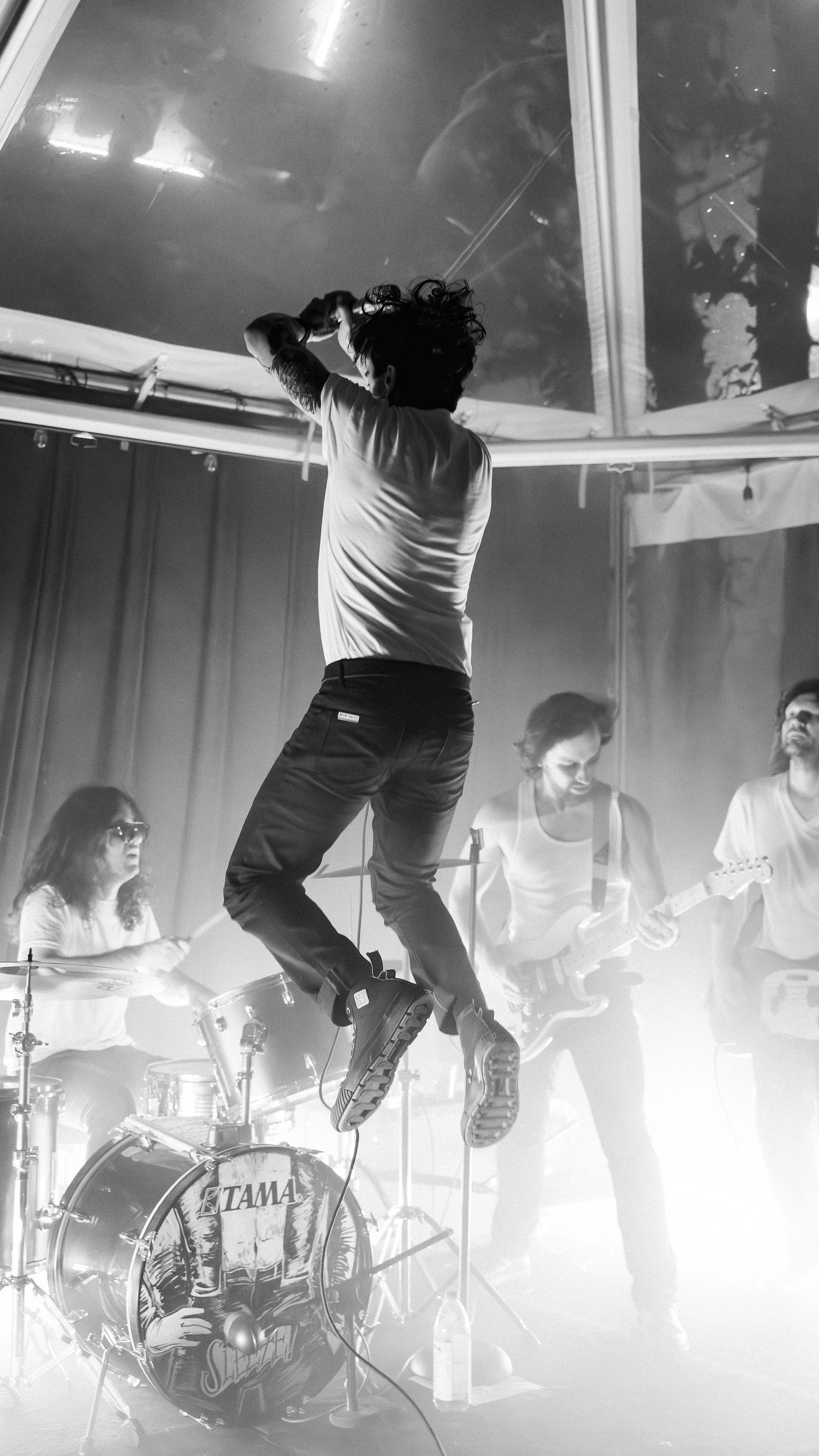 Black and white photo of performer jumping high during energetic concert with band playing.