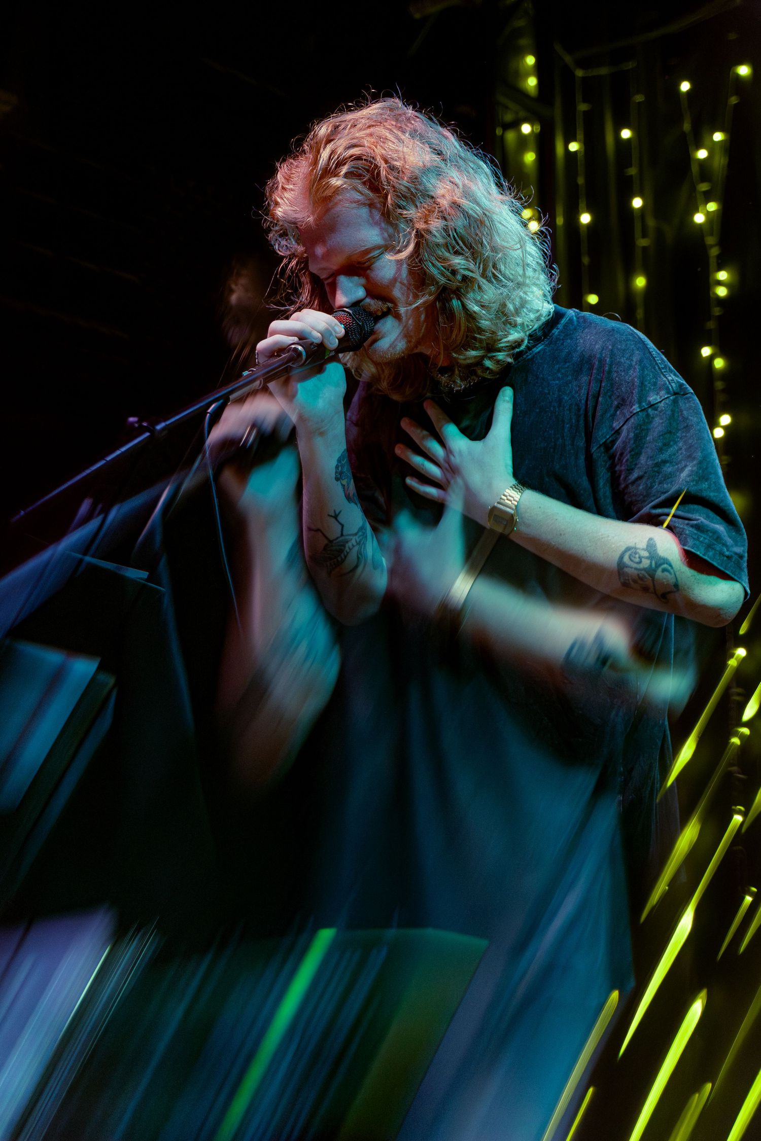 Silhouette of a performer passionately singing on stage with dramatic blue and green lighting in the background.