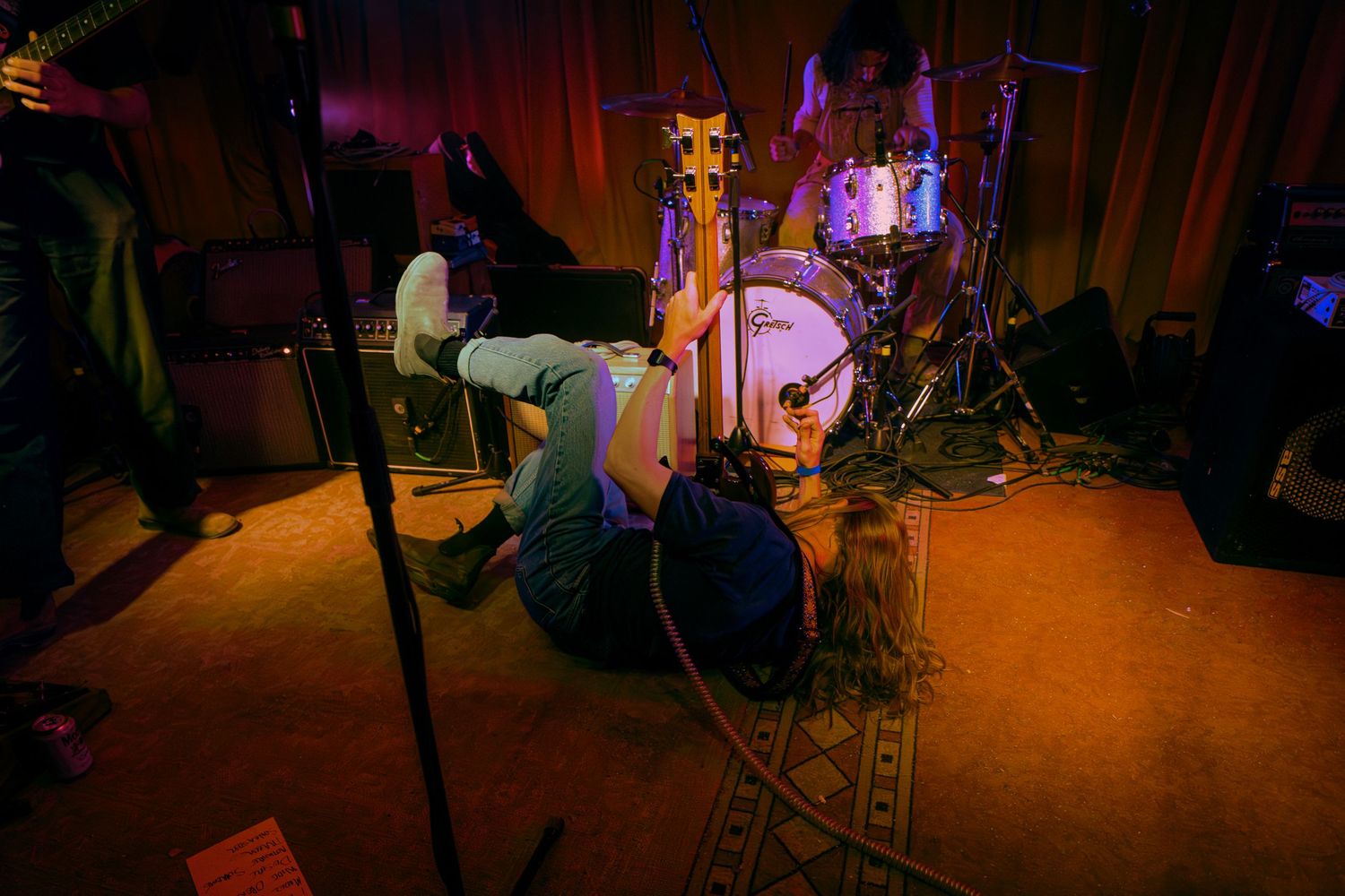 A musician performs on stage in a dimly lit venue with orange and purple lighting creating a moody atmosphere.