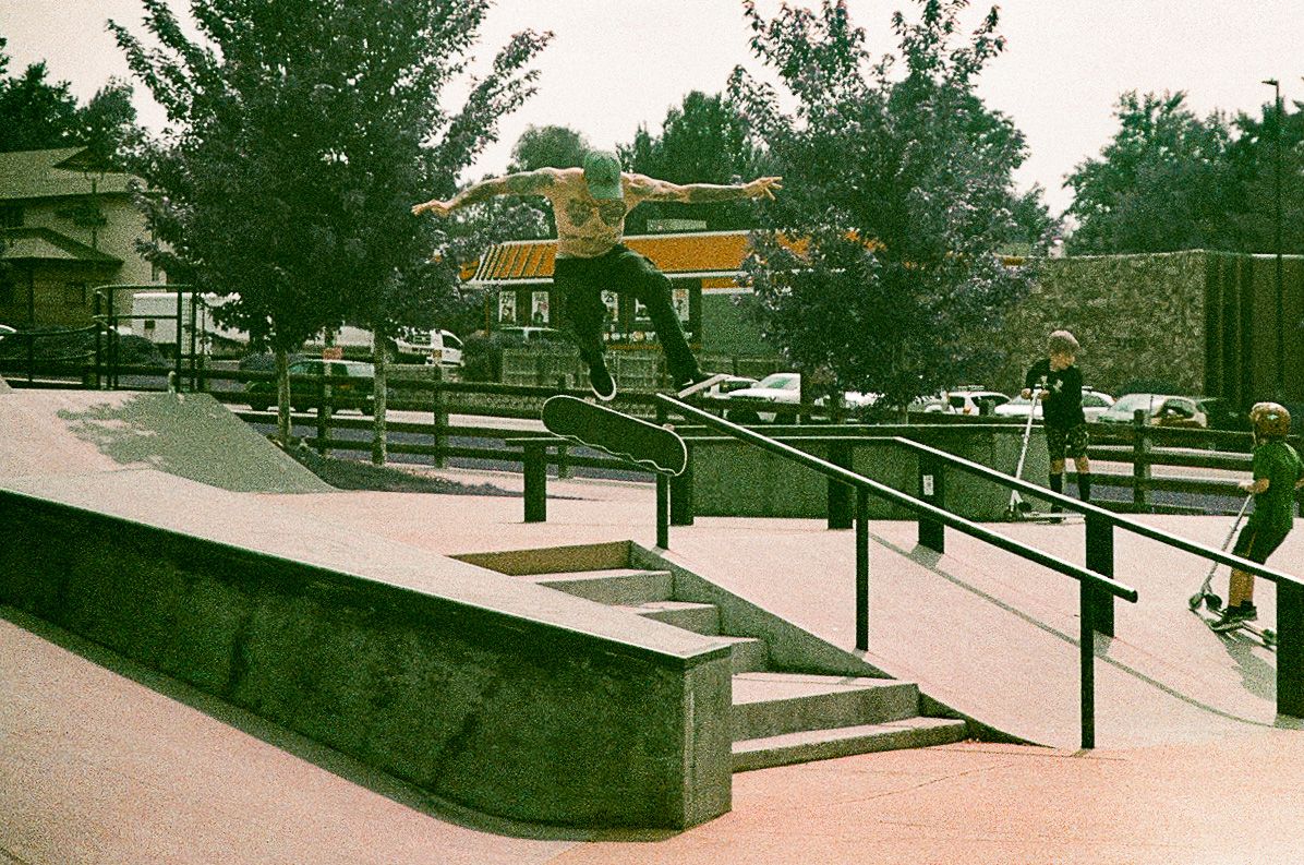 Skateboarders practicing tricks at a concrete skate park with handrails and steps.