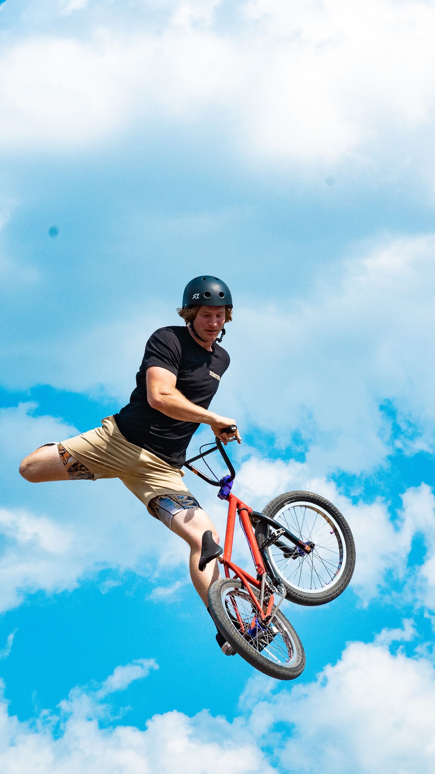 BMX rider executes sideways aerial maneuver with red bike against bright blue sky.