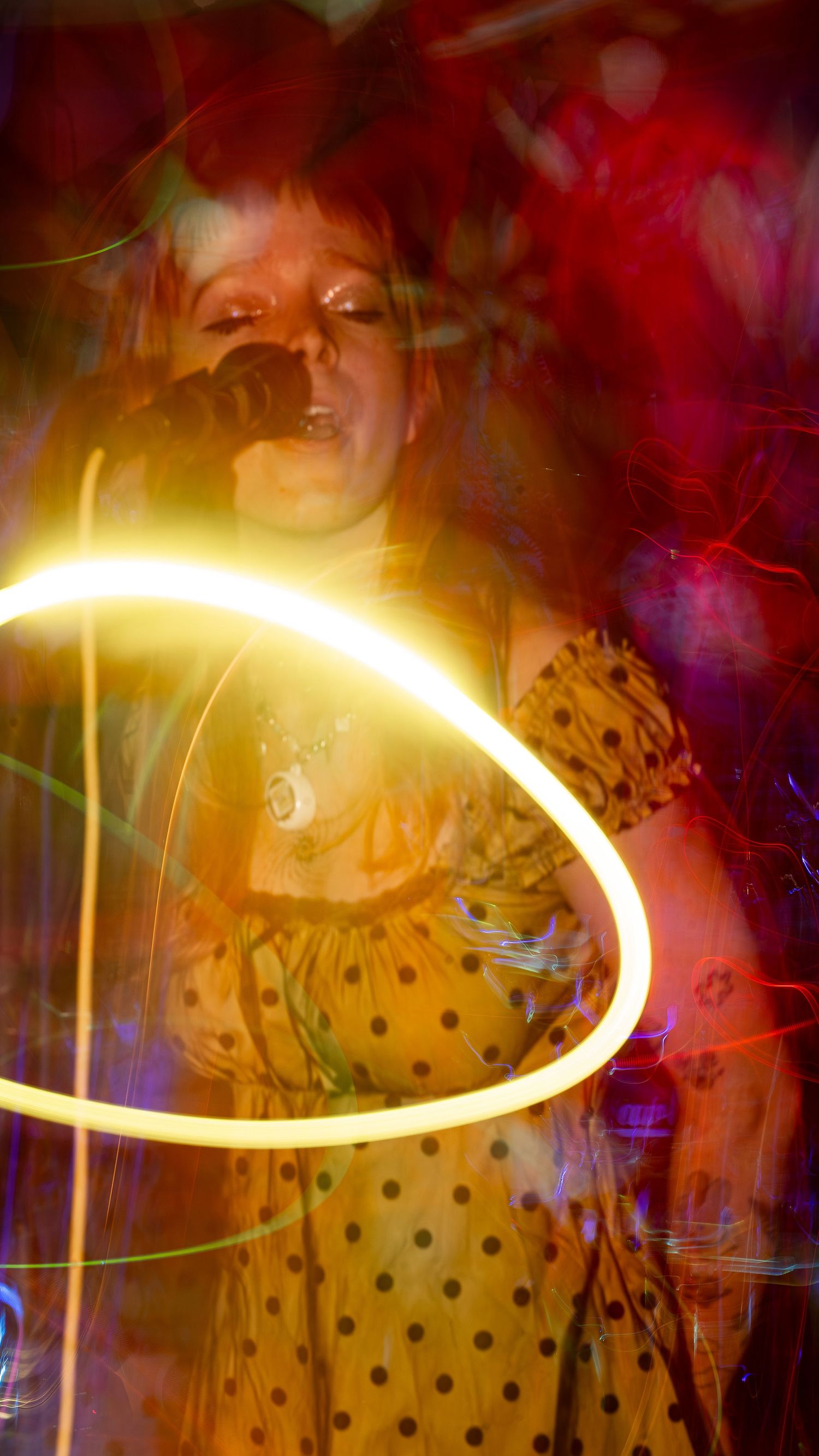 Singer in polka dot dress performing under swirling orange and purple stage lights.
