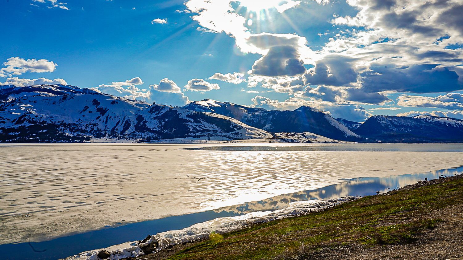 Wide panorama of snow-covered mountains with dramatic clouds and sunlight.