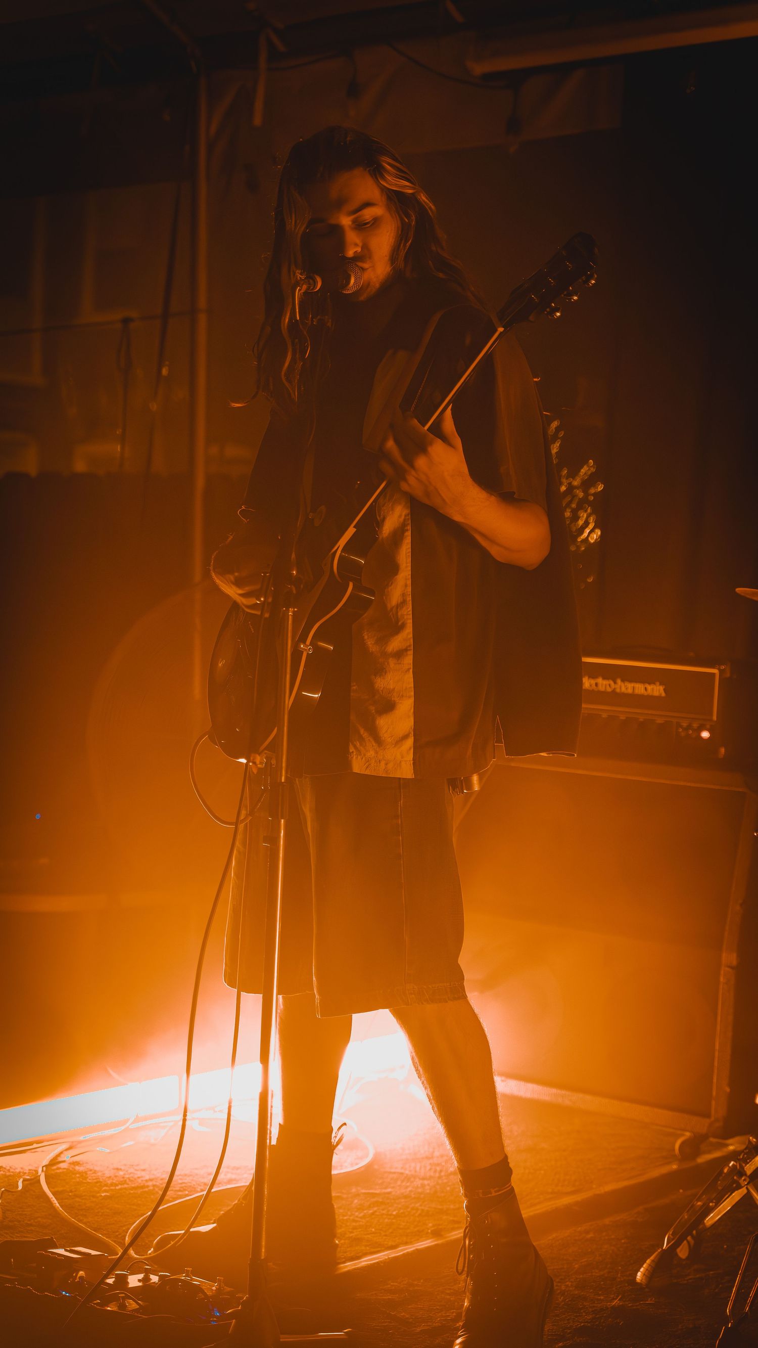 Musicians performing on stage illuminated by warm orange spotlights during intense concert moment.