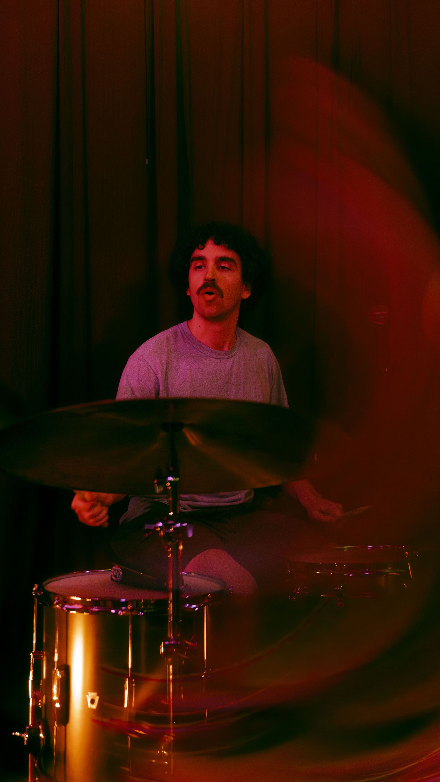 Drummer performs on stage bathed in dramatic red lighting while playing an energetic set at a live music venue.