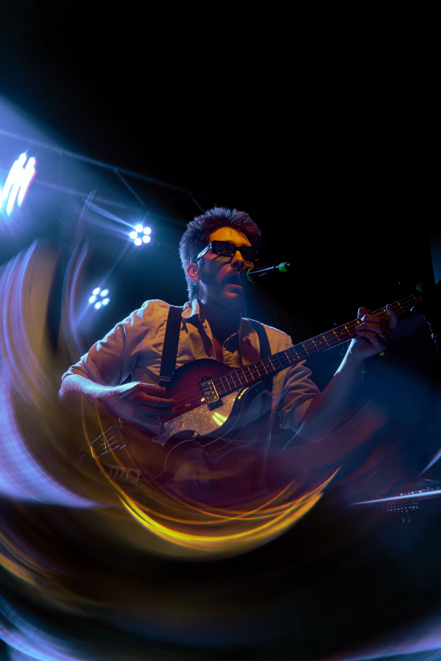 A guitarist performs on a dimly lit stage with dramatic blue lighting creating swirling motion effects during a live concert.