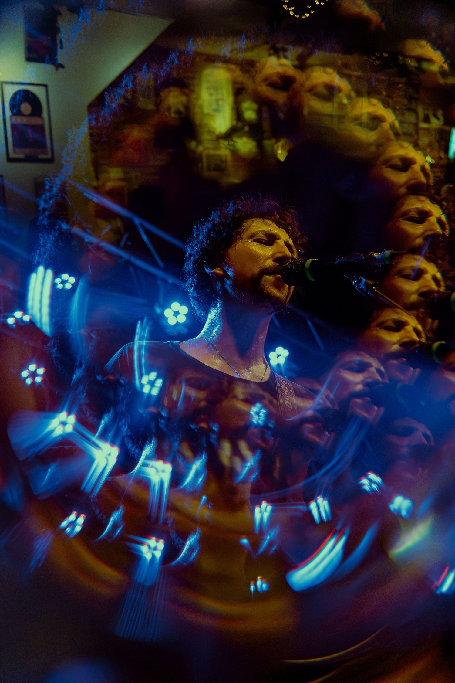 Long exposure photograph shows glowing blue and white flowers in a dark scene creating light trails and ghosting effects.