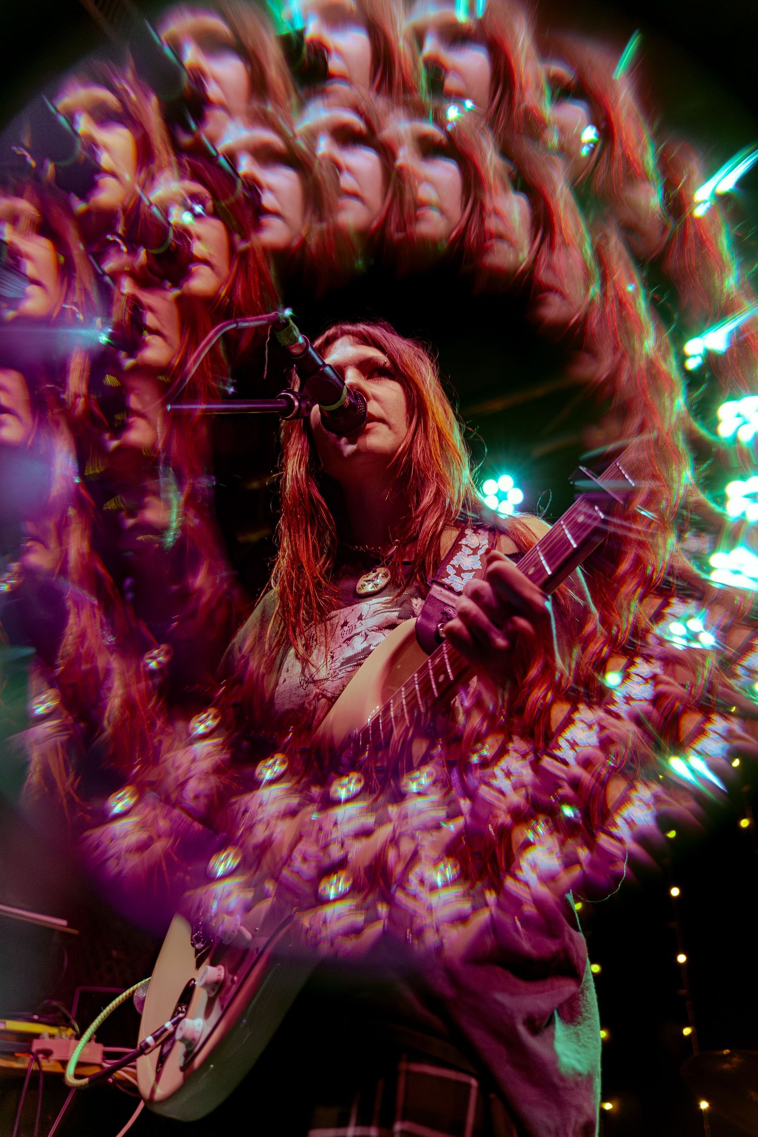 Kaleidoscopic concert photo shows musician playing guitar with spiraling visual effect and colorful stage lighting.