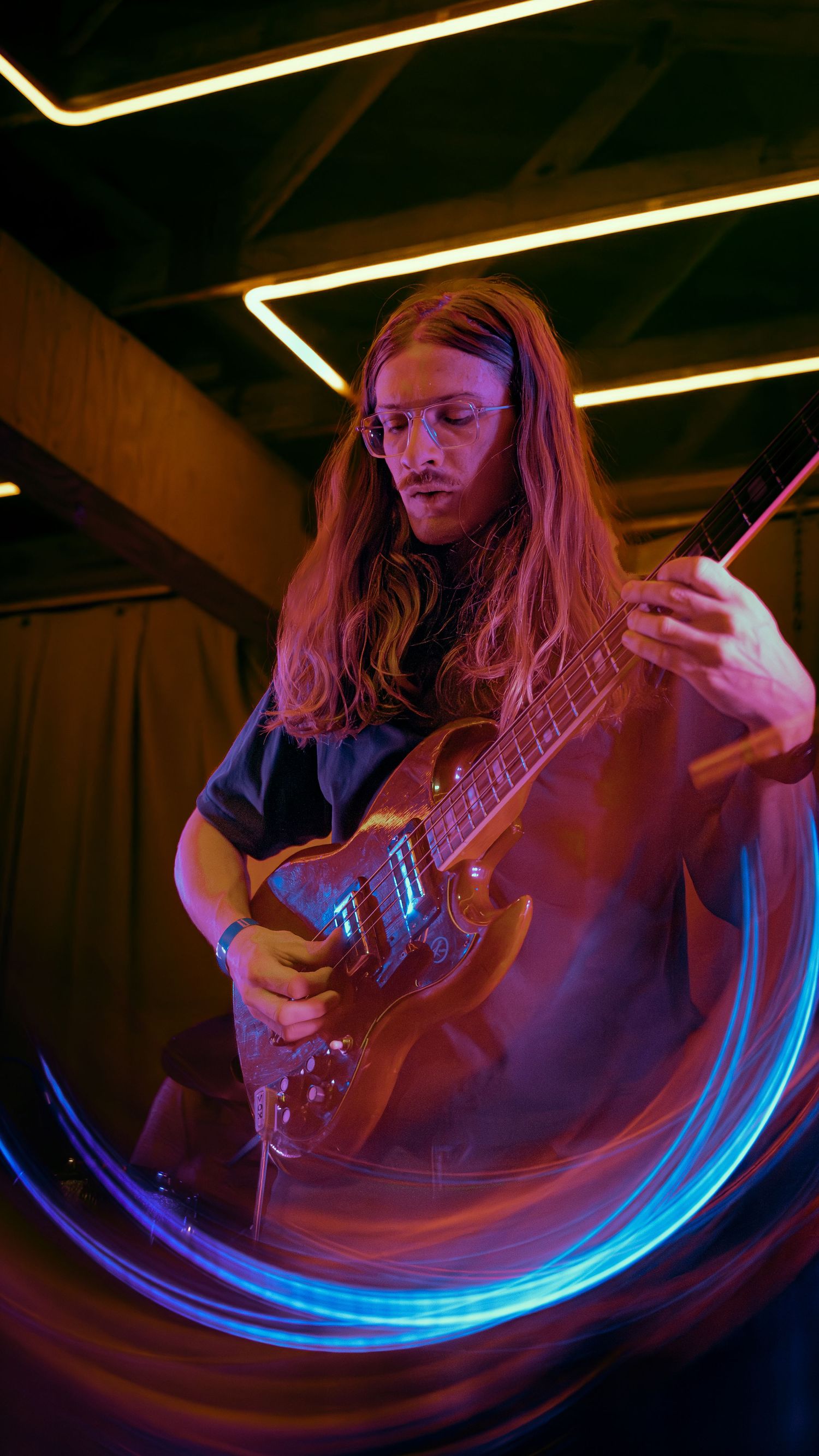 A guitarist performing under dramatic red and blue lighting creates swirling motion blur effects during a live performance.