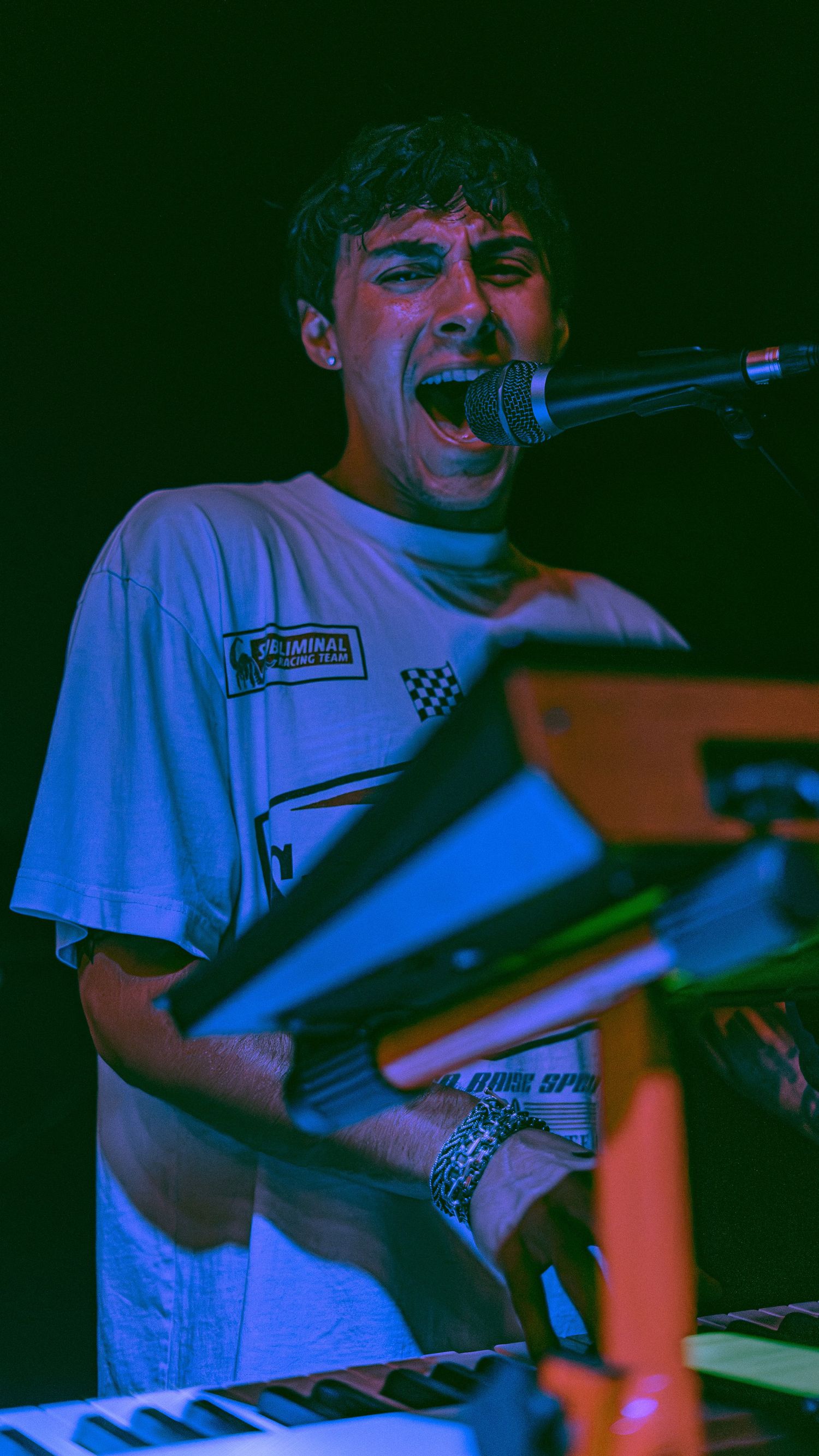 A musician performs energetically on stage bathed in dramatic blue and red lighting.