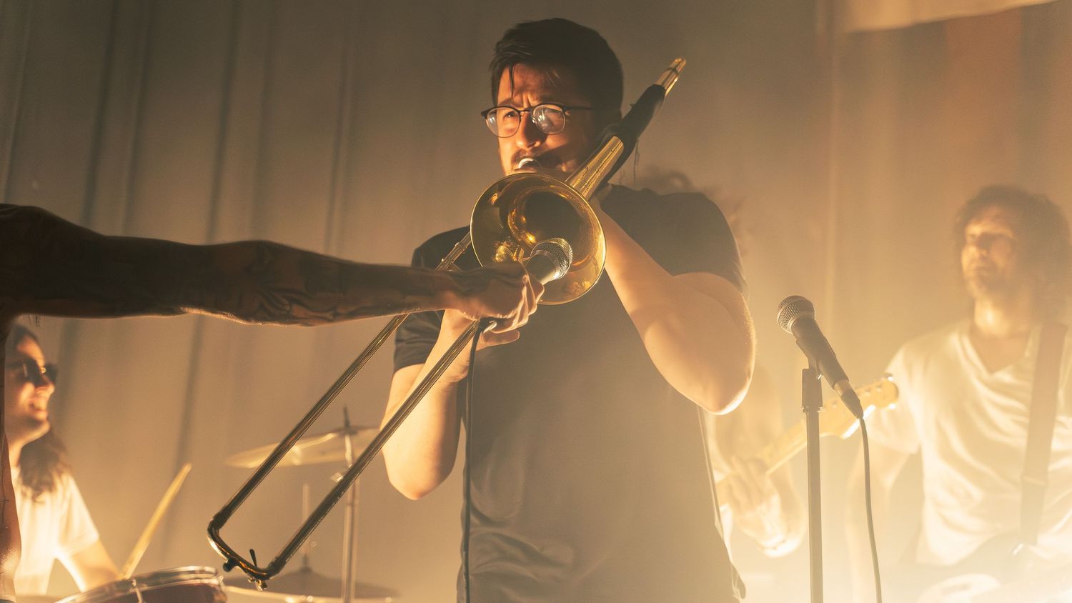 Rock band performs energetically on stage with dramatic warm lighting creating an atmospheric concert scene.