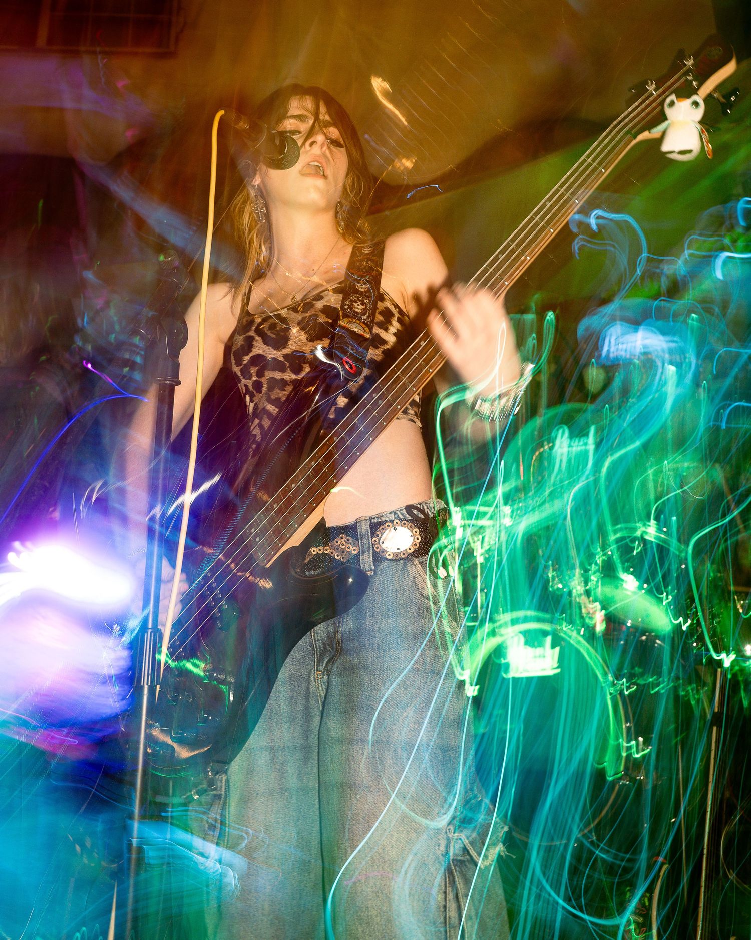 Musician playing guitar amid swirling green and blue stage lights creating ethereal atmosphere.